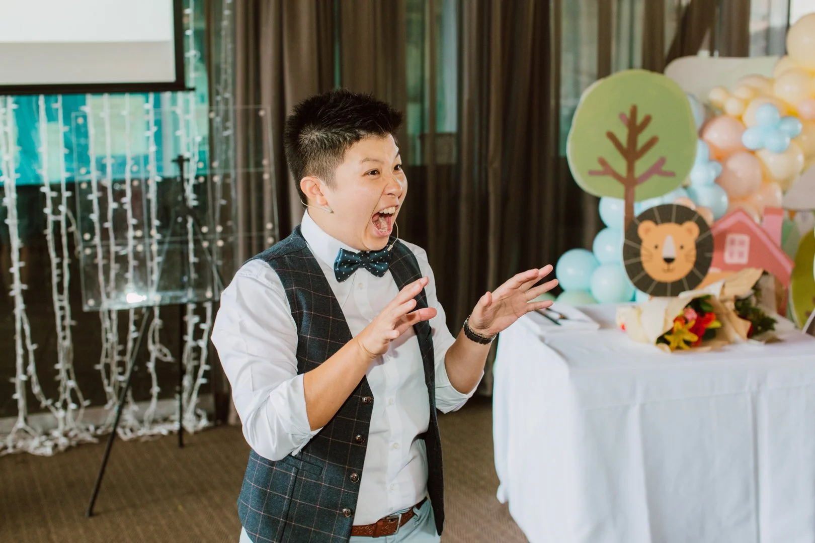 Person speaking passionately at a decorated event, with colorful balloons and cartoon animal and nature cutouts in the background