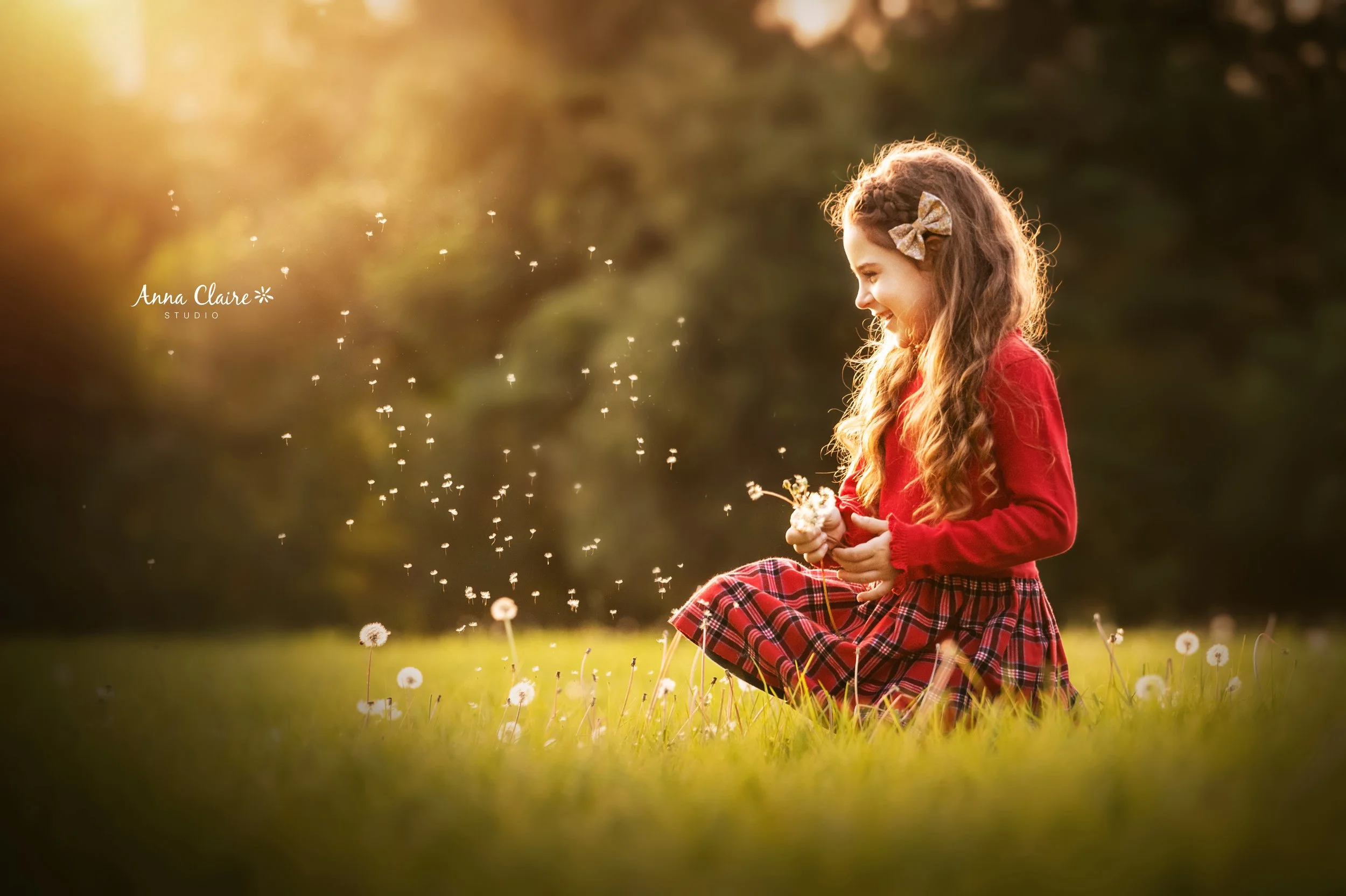 A young girl with long curly hair, wearing a red jacket and a plaid skirt, sitting on the grass in a field of dandelions during sunset, blowing on dandelions and smiling.