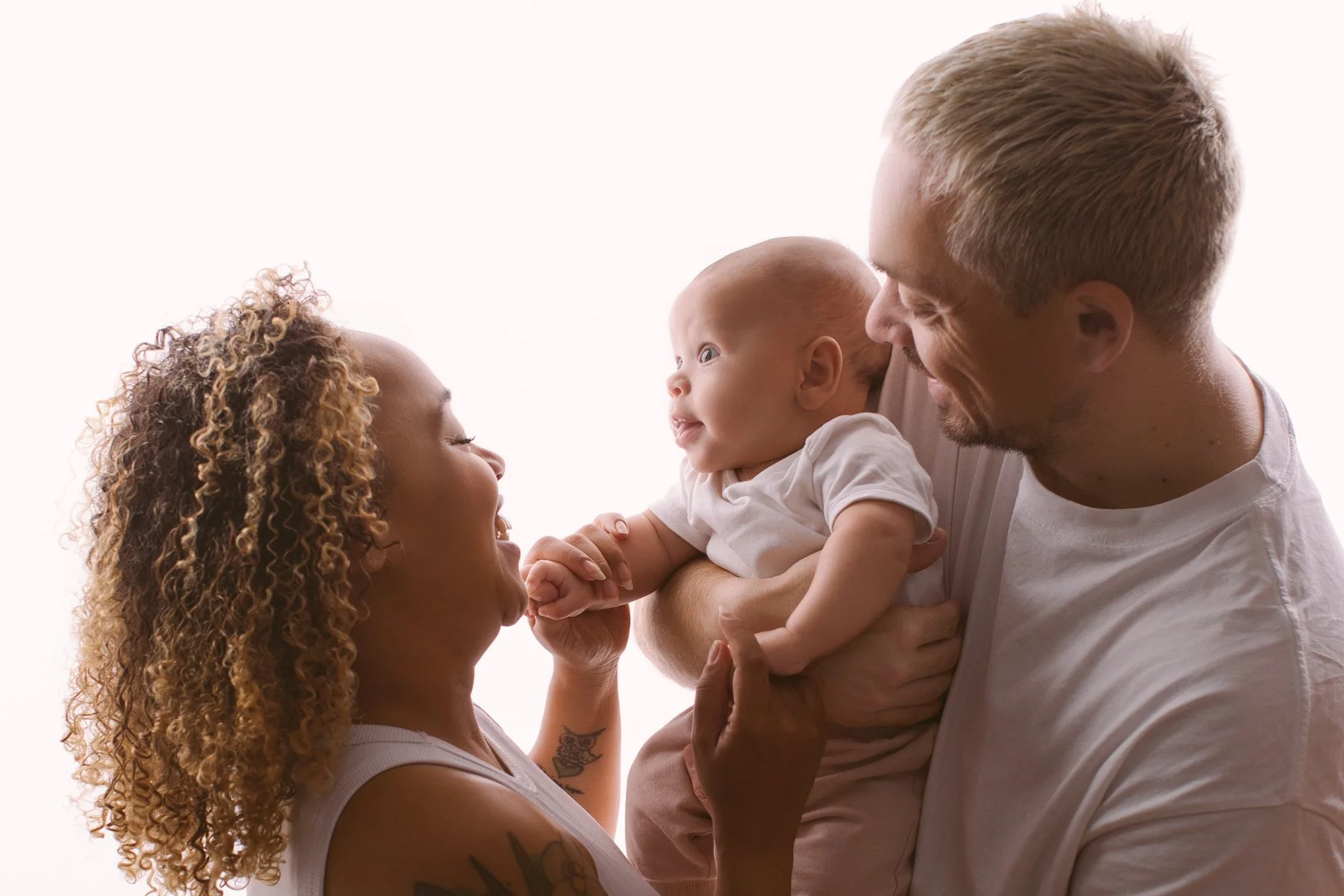 A diverse family with a woman, man, and baby happily interacting against a white background.