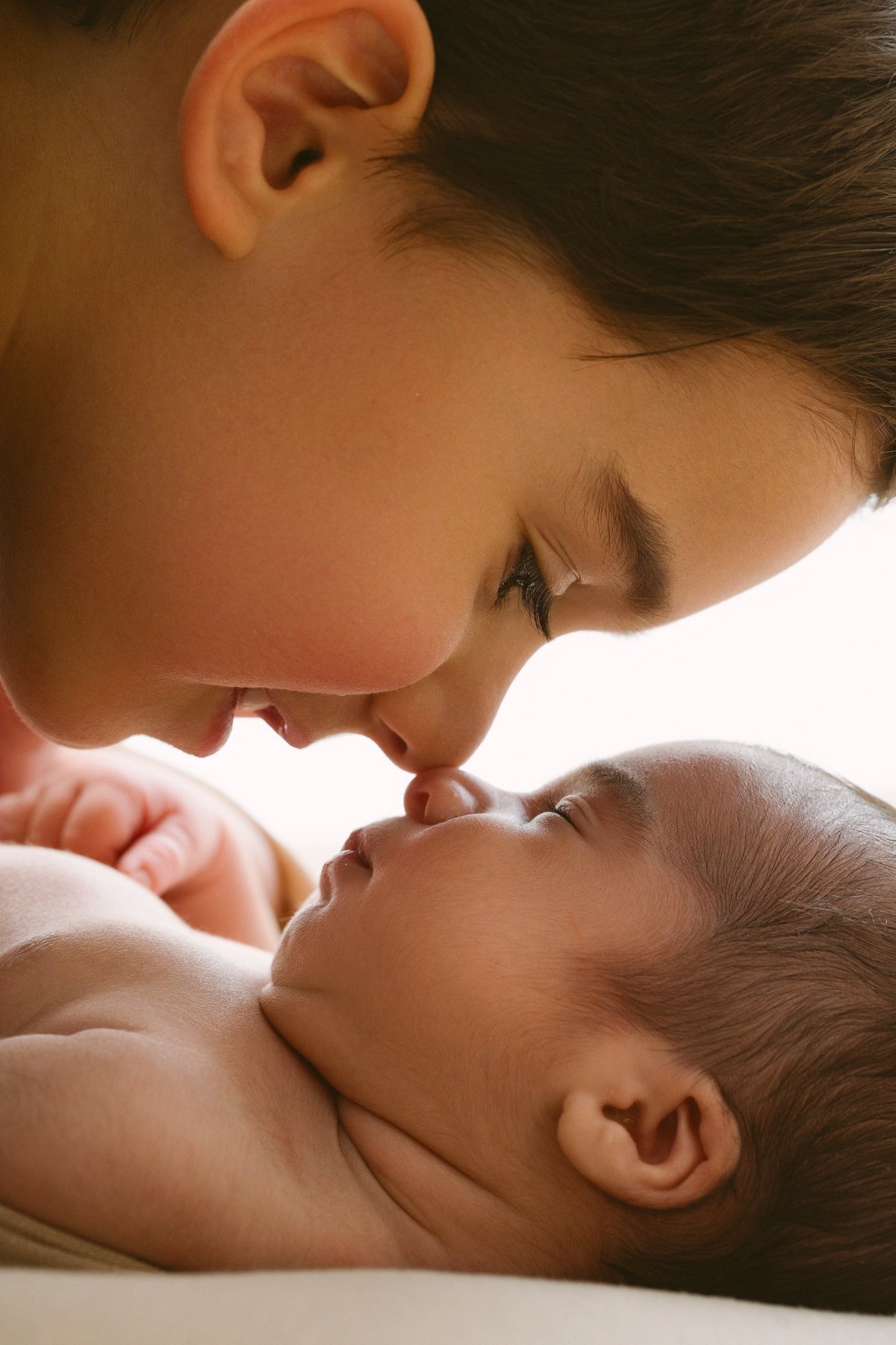 in this sibling photo, The older brother gently touching his forehead to a baby boy's nose during an intimate close-up moment.