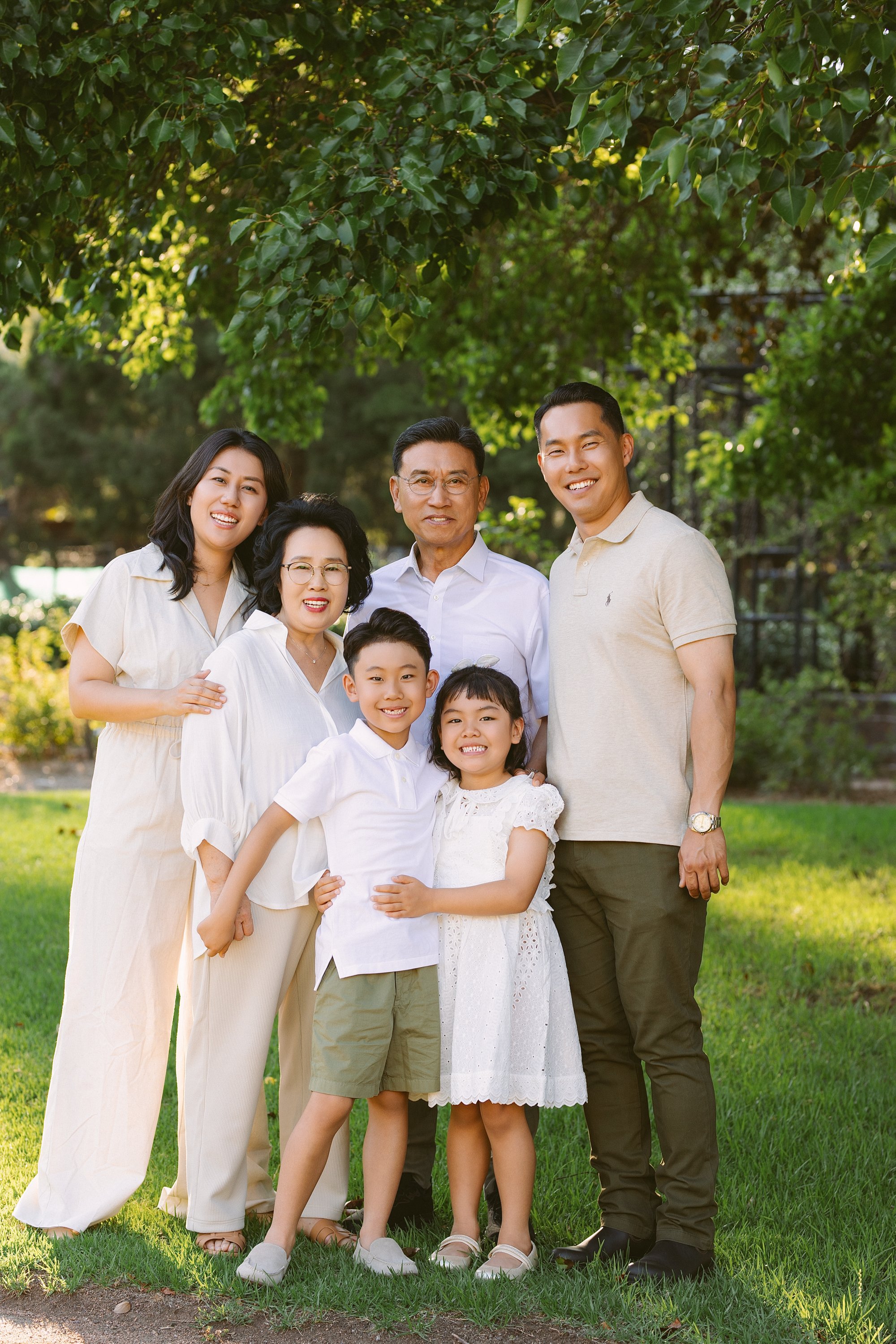 Family photo of seven people standing outdoors on grass, smiling, with trees in the background.