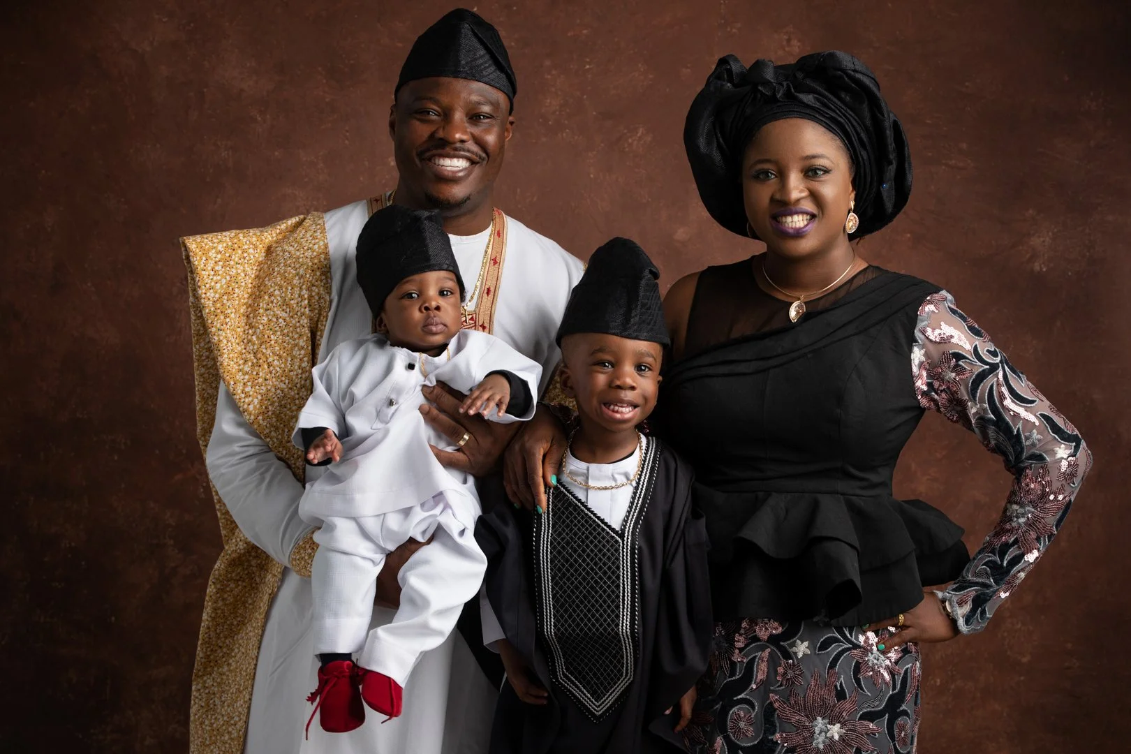 A family portrait of a Nigerian family dressed in traditional attire, with a father, mother, and two children, standing against a brown backdrop.