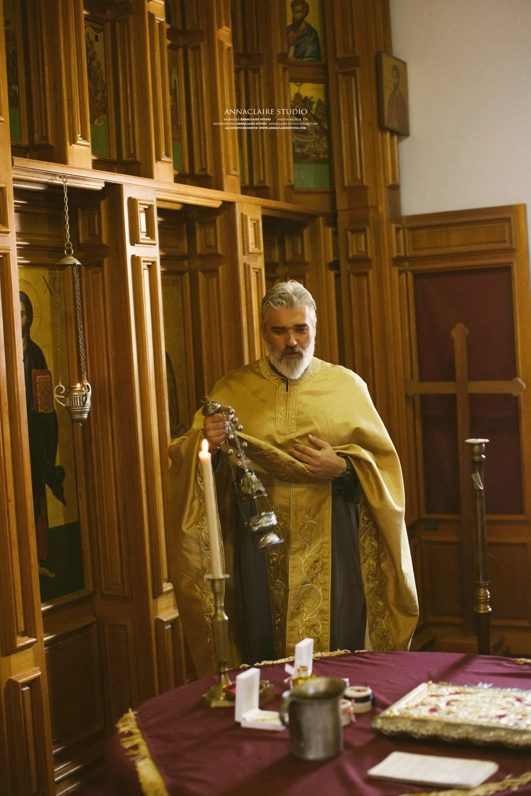 An Orthodox priest in gold vestments holding a censer in an ornate wooden church interior.