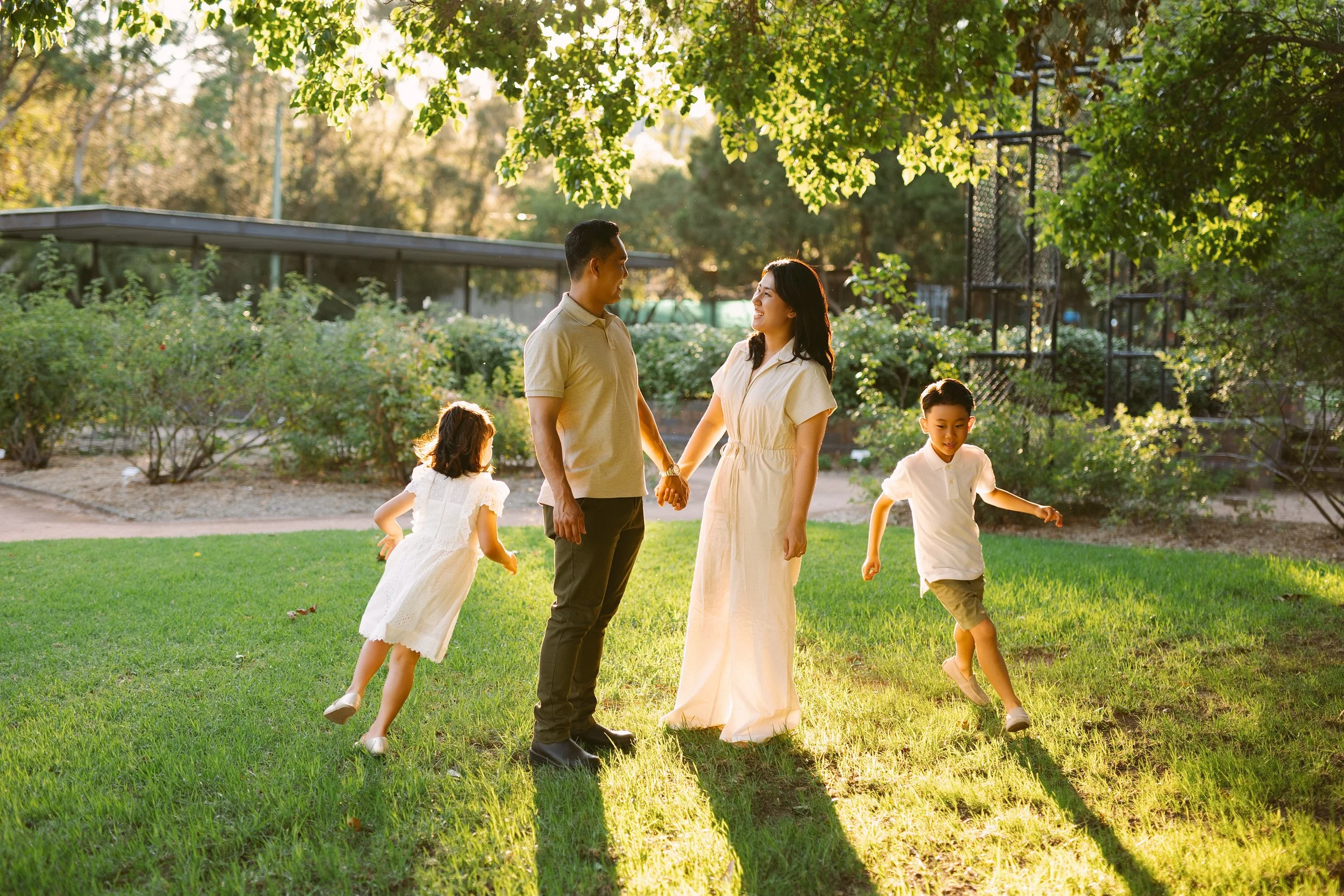 A family of four, including a man, woman, and two children, enjoying a walk in a park during sunset with trees at parramatta park