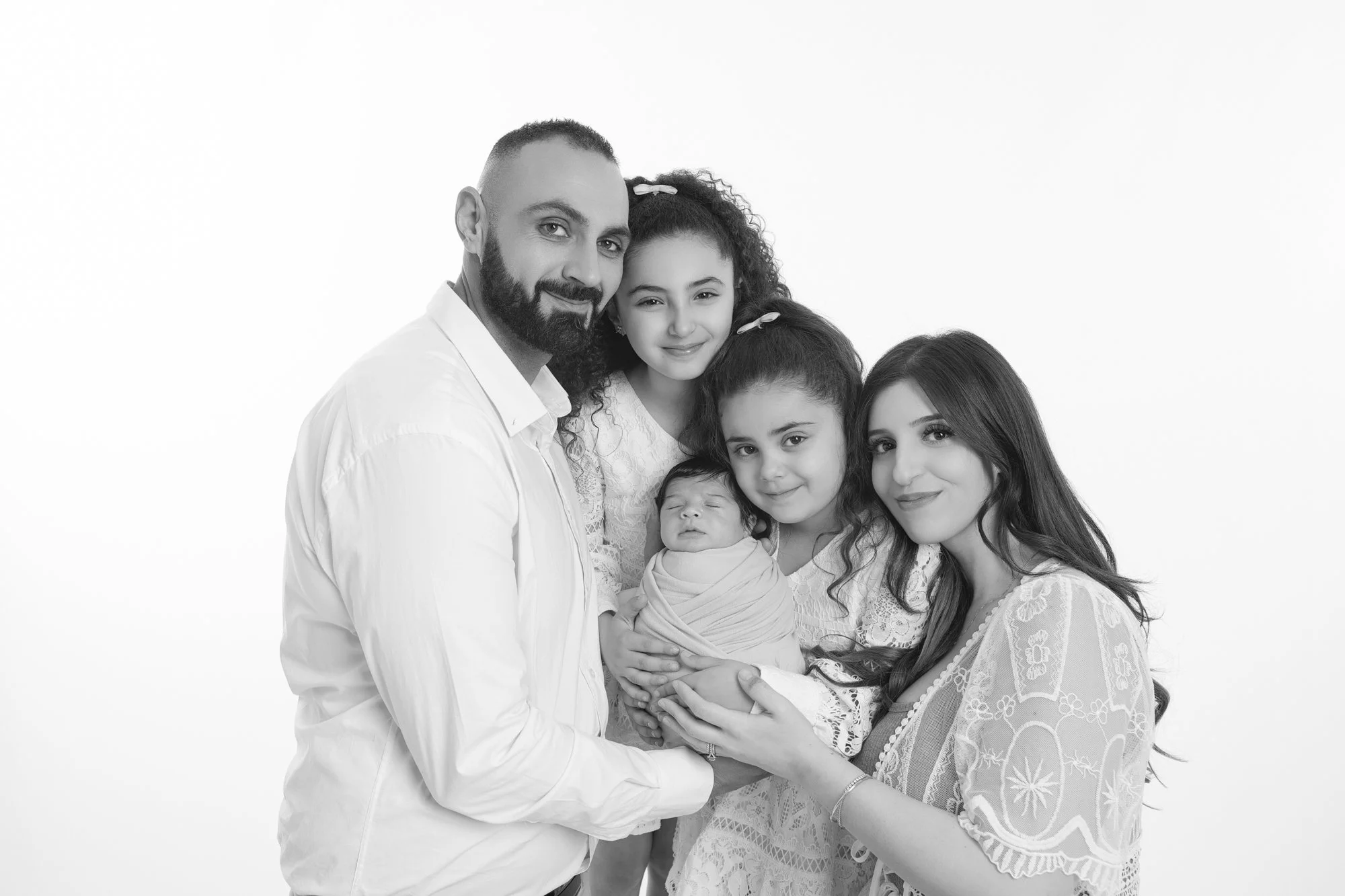 A black-and-white family portrait with five members, including two young girls, a woman, a man, and a newborn baby.