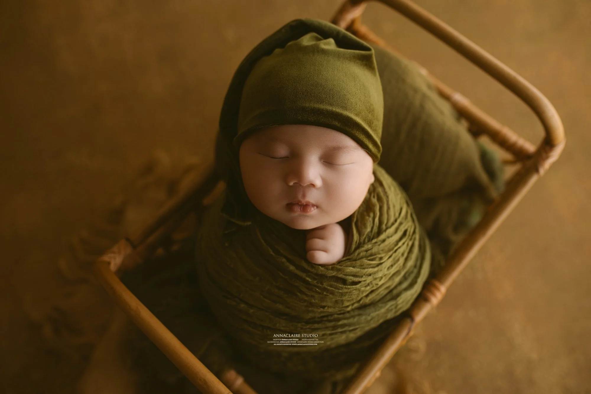 A sleeping baby wrapped in green fabric, lying in a small wooden basket.
