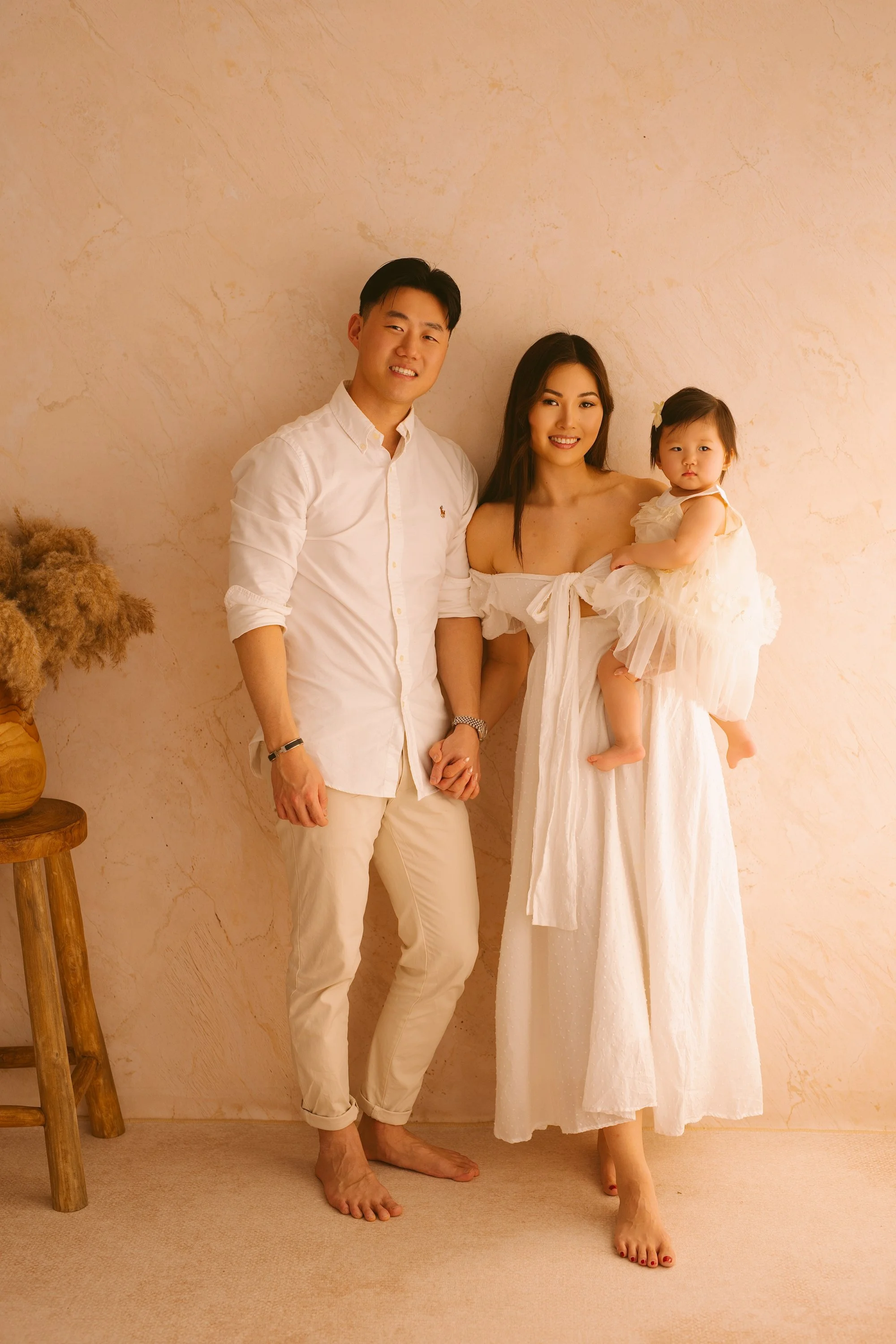 Woman holding a smiling baby, father looking at them, intimate family moment.