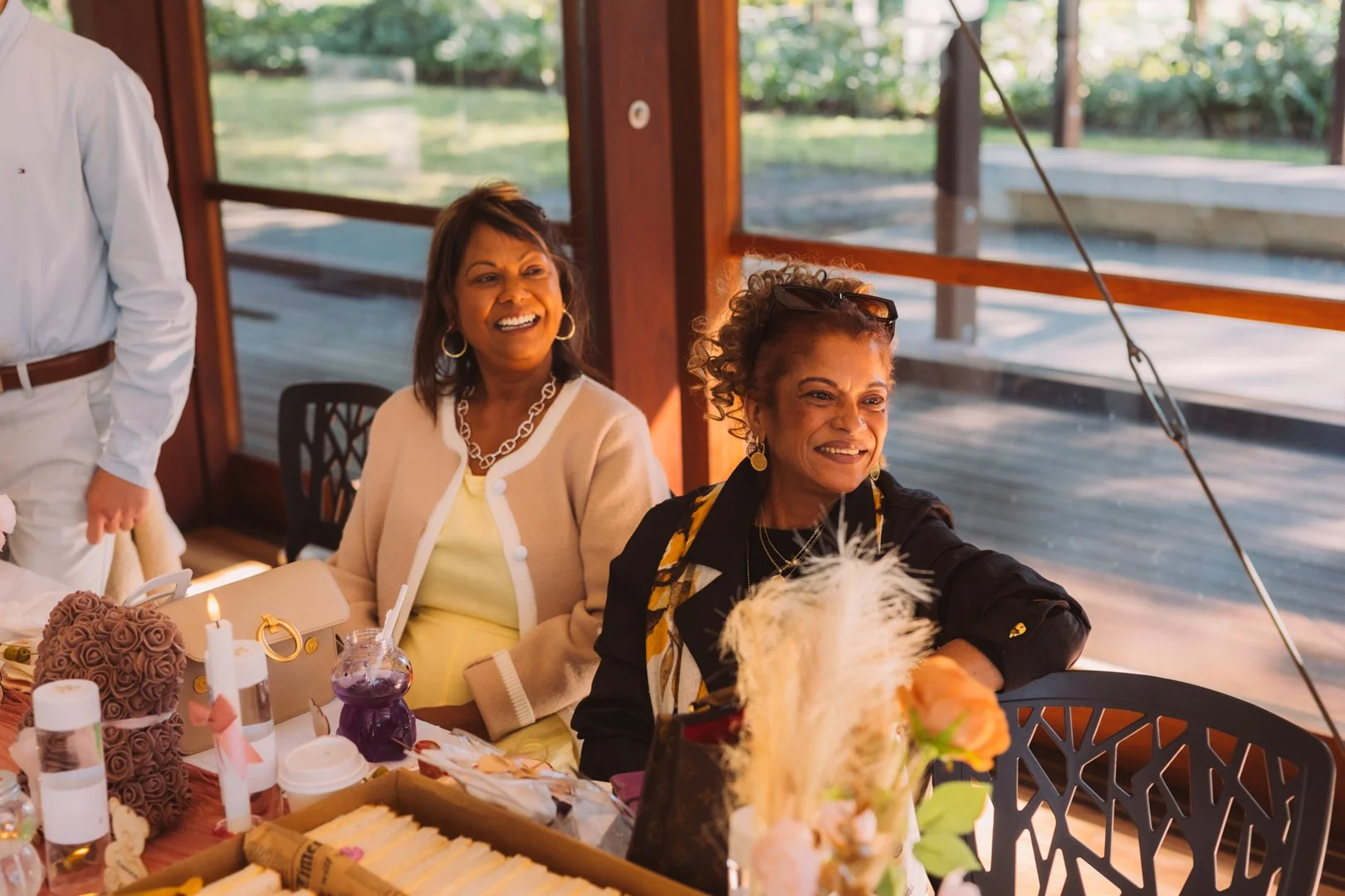 Two women sitting at a table, smiling and enjoying themselves at a social gathering or celebration.