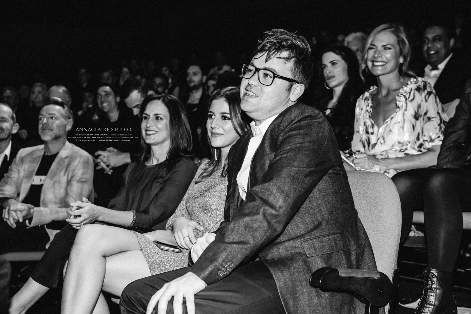 People sitting in an audience at a formal event, dressed in business or semi-formal attire, smiling and clapping.