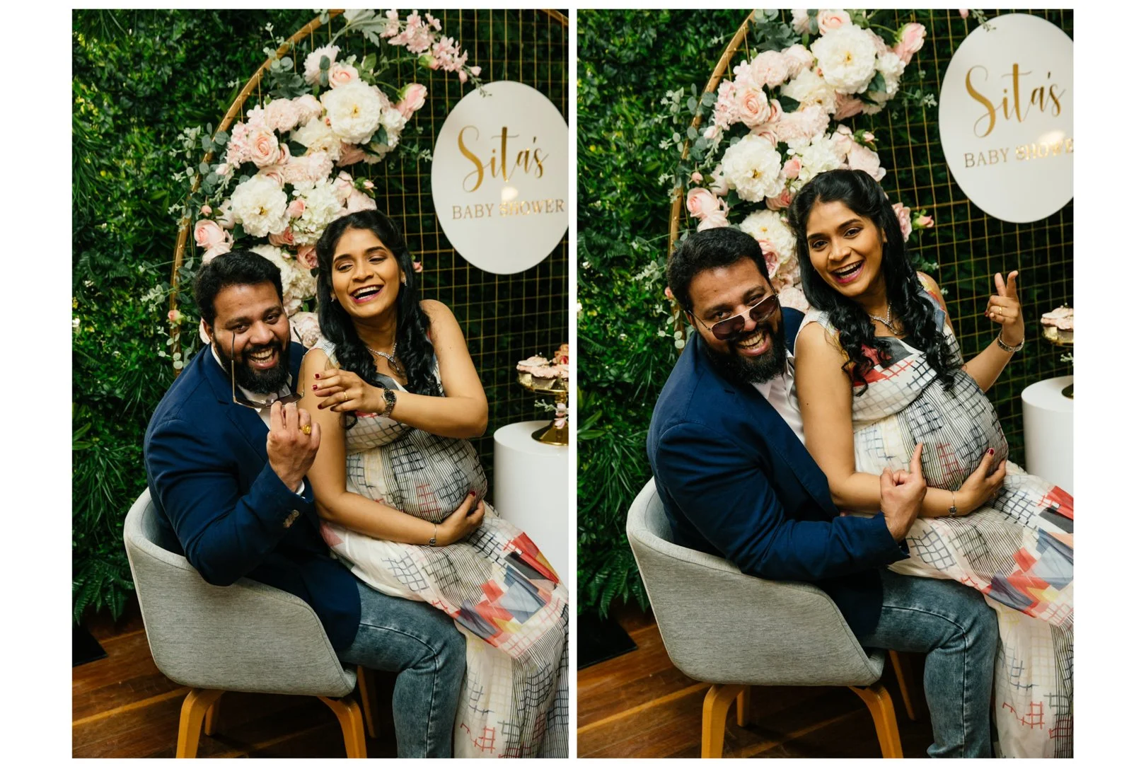 Two people smiling and posing at a baby shower, with a floral backdrop and a sign that says "Sita's Baby Shower." One person is a pregnant woman wearing a patterned dress, and the other is a man wearing a navy blazer and glasses.