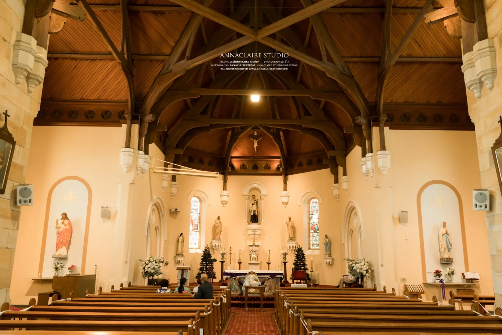 Interior of a church with wooden pews, statues, stained glass windows, and an altar.