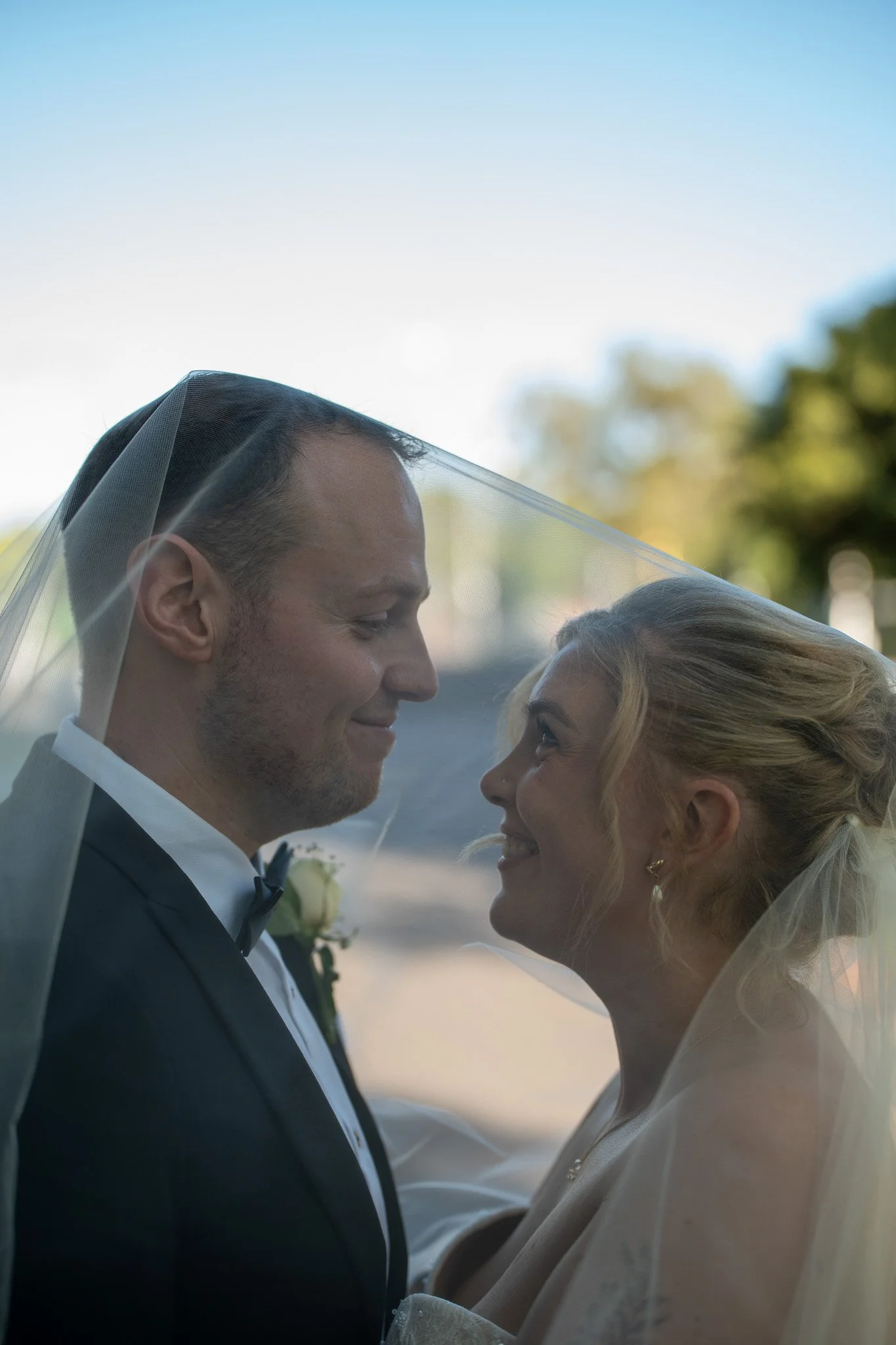 A bride and groom sharing a close moment with their foreheads touching, smiling, during their wedding ceremony outdoors on a sunny day.