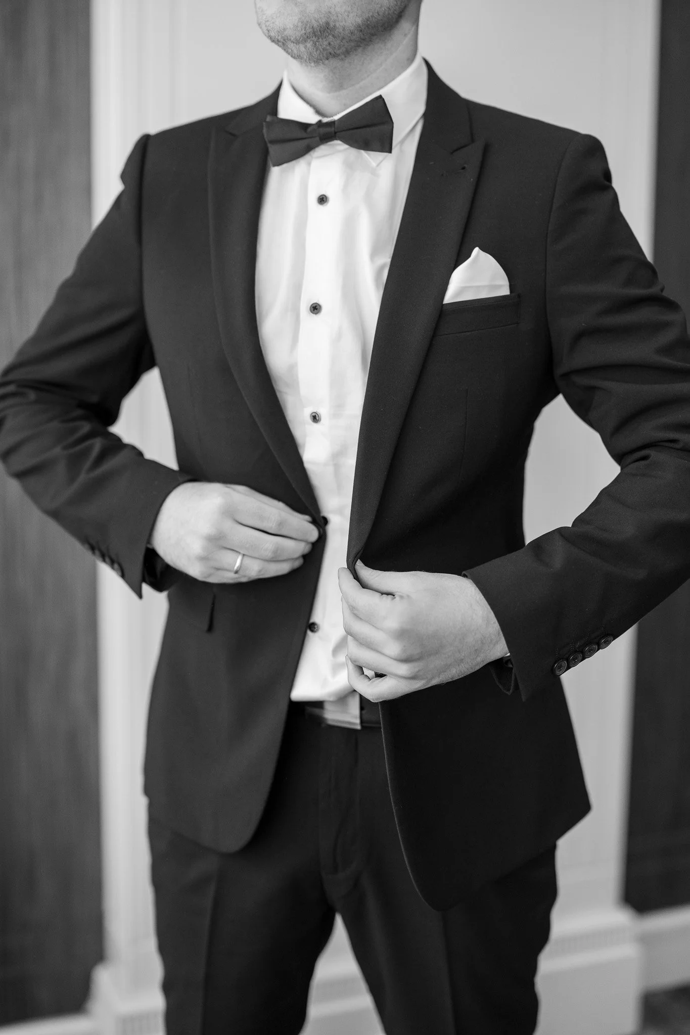 A man in a tuxedo adjusting his jacket.