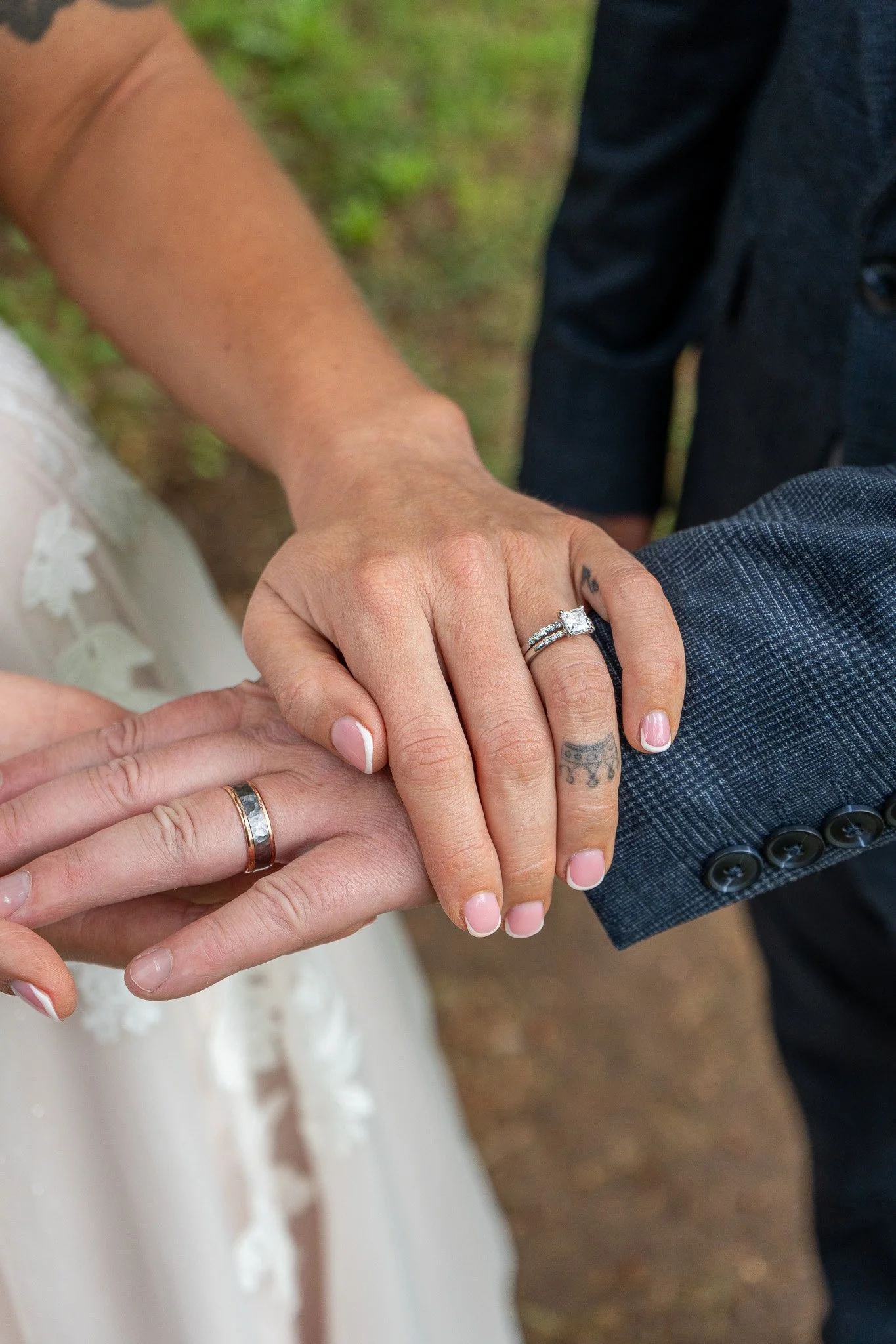 Close-up of a couple holding hands during a wedding ceremony, showcasing wedding rings and tattoos, with blurred background.