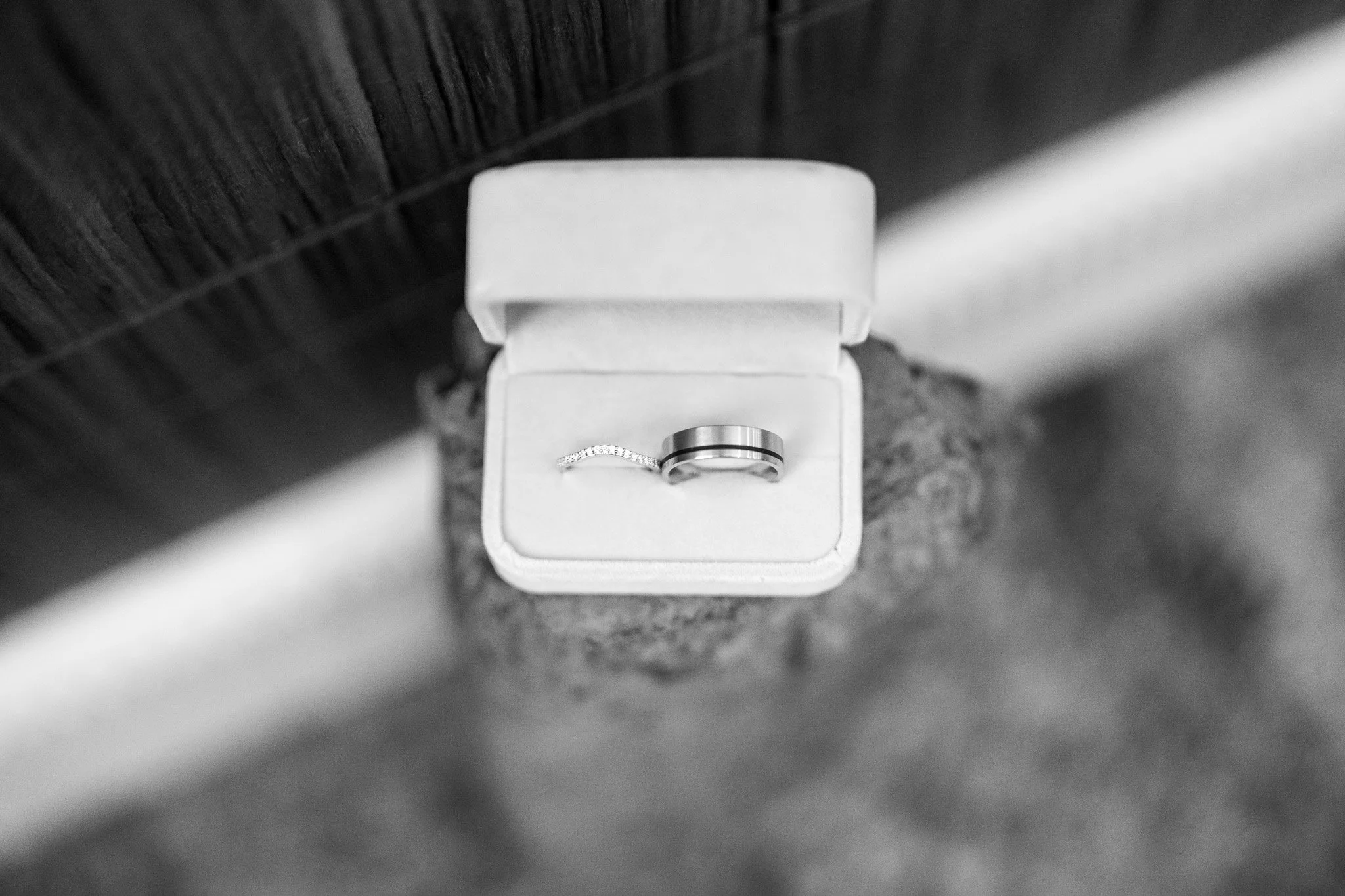 A ring with a black band and a diamond wedding band in a white jewelry box.