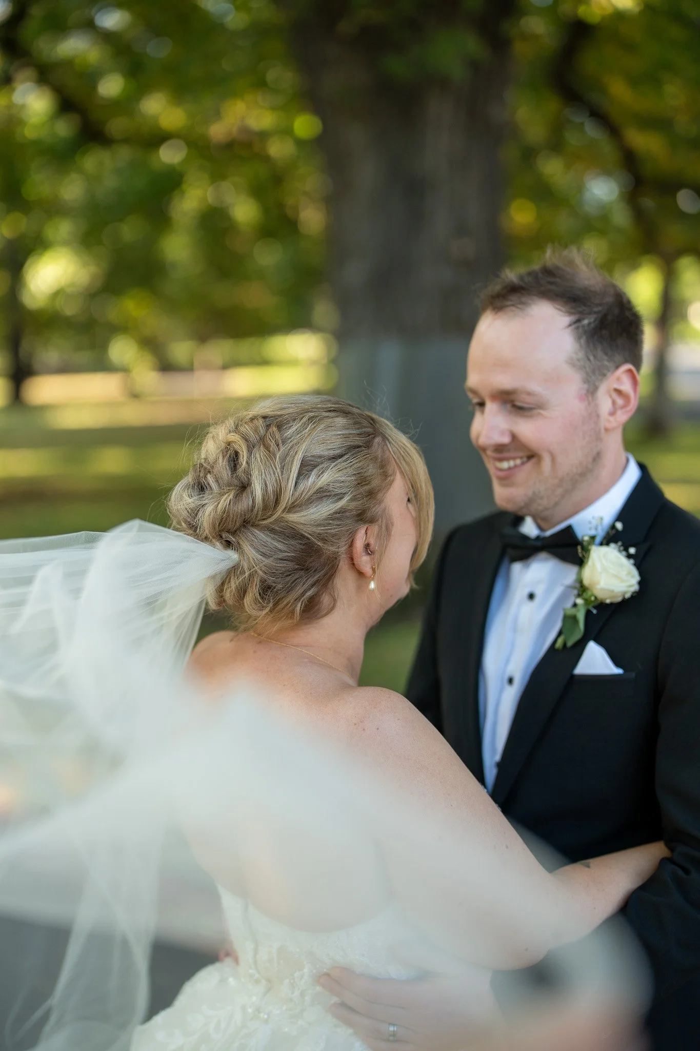 A bride and groom share a joyful moment during their wedding outdoors, with trees and greenery in the background.