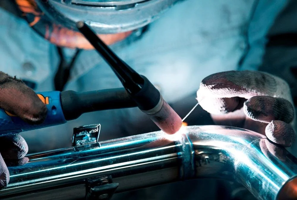 A person welding a metal pipe with a welding torch, wearing gloves and protective gear.