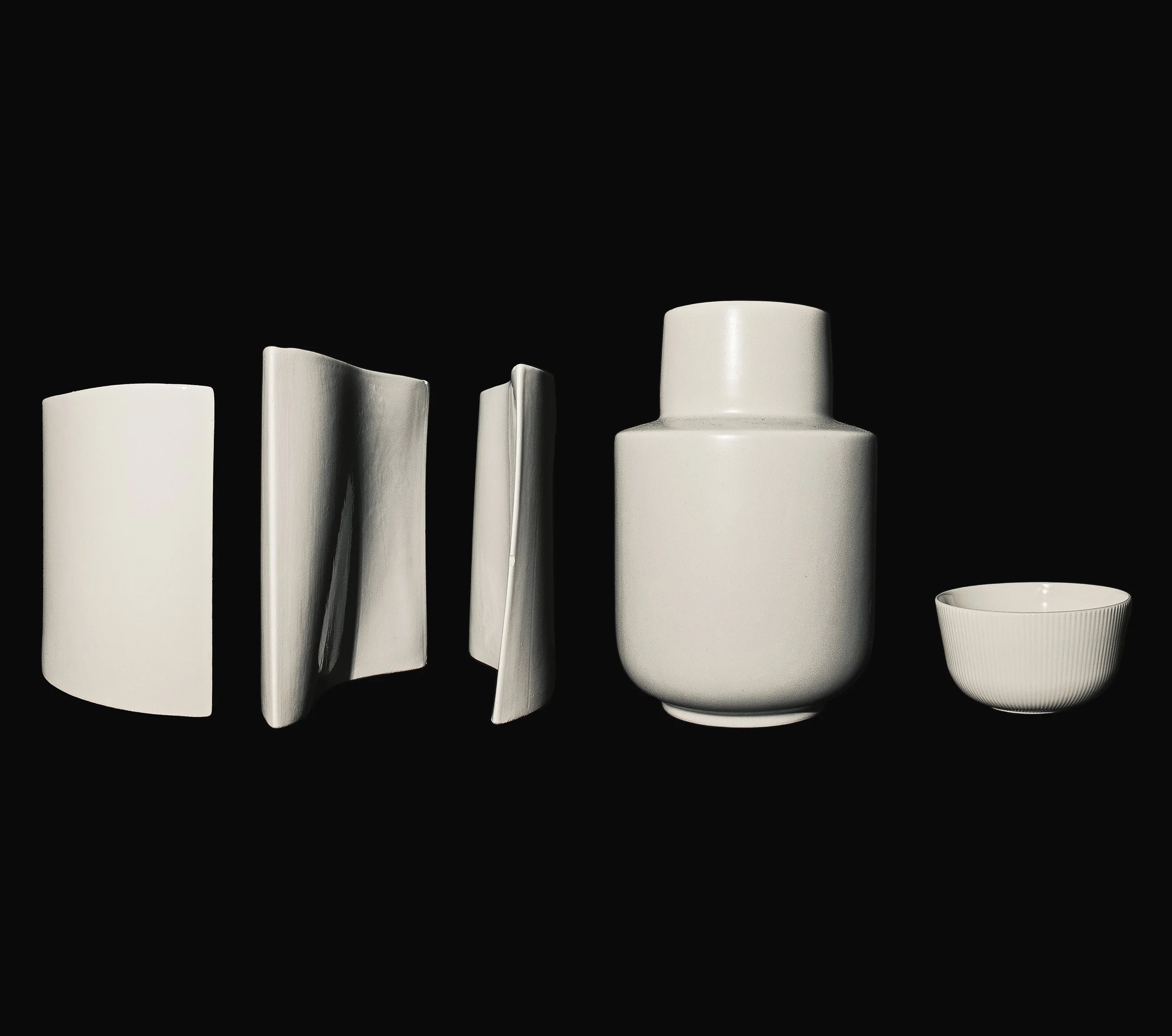 Arrangement of white ceramic vases and bowls on a black background.