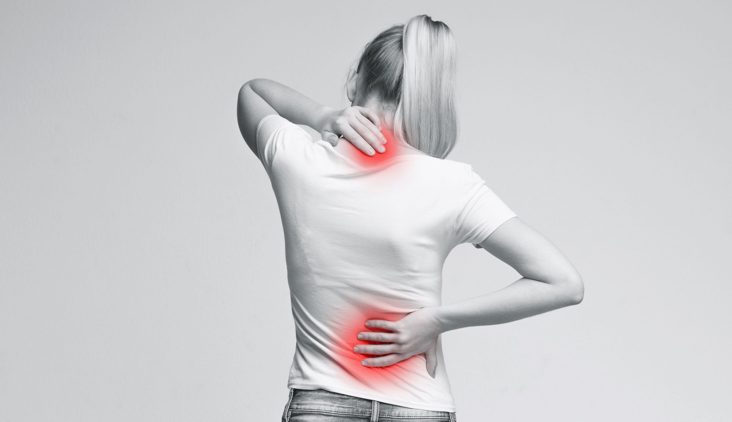 Black and white photograph of a woman holding her lower back with subtle red highlighting over the sacroiliac joint region, illustrating inflammatory back pain.