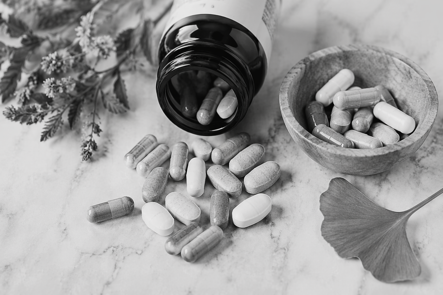 Black and white close-up photograph of supplement capsules and tablets spilled from a bottle, used to illustrate a blog on supplements in rheumatology and bone health.
