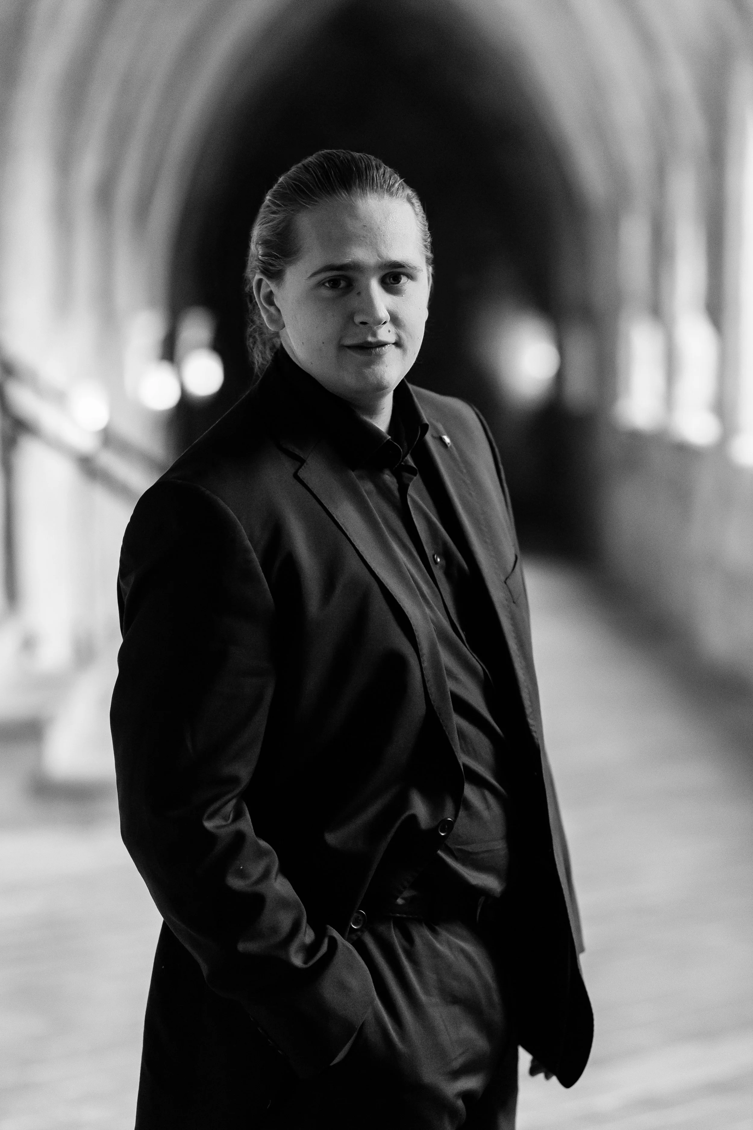 Schwarz-weiß-Foto eines jungen Mannes in einem Anzug mit offenem Hemd, der in einem Tunnel steht und in die Kamera schaut.