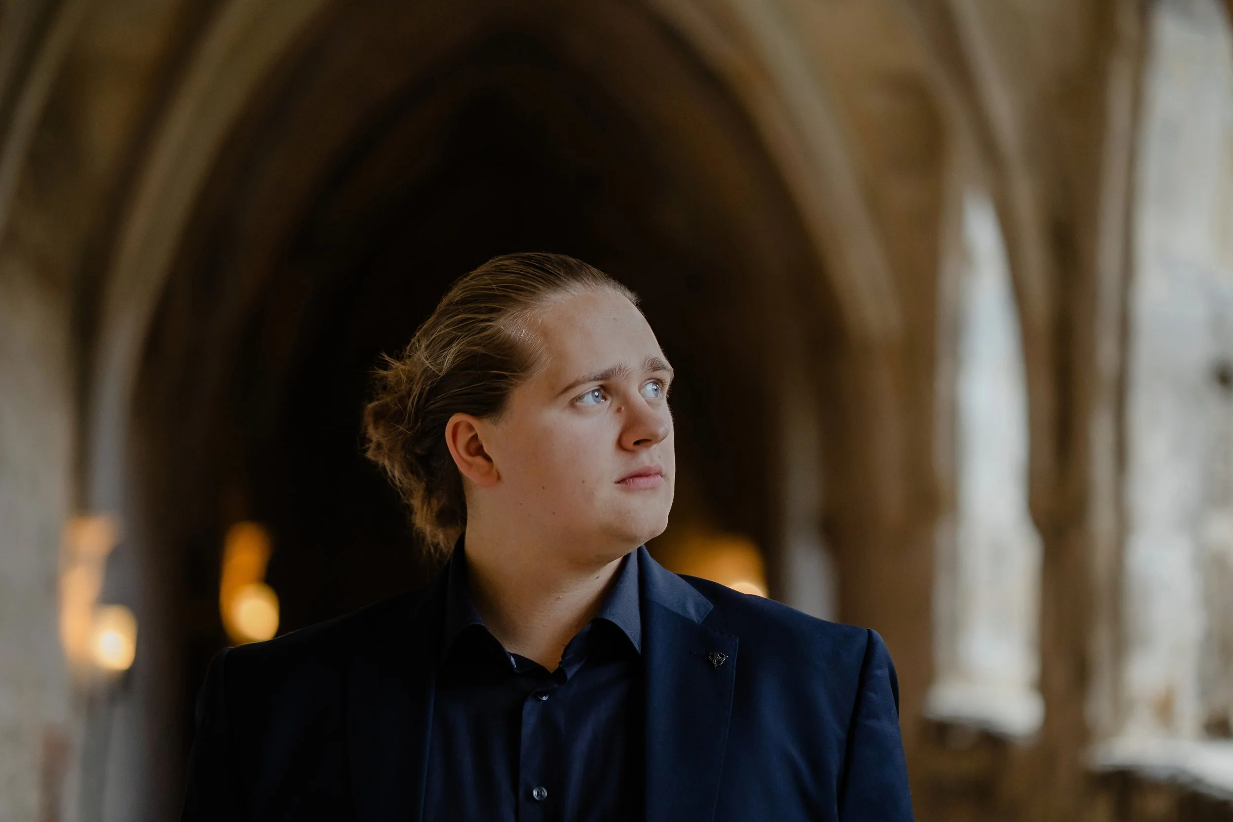 Junge Frau mit blauen Augen und dunkler Kleidung in einem gotischen Tunnel, blickt nach rechts.