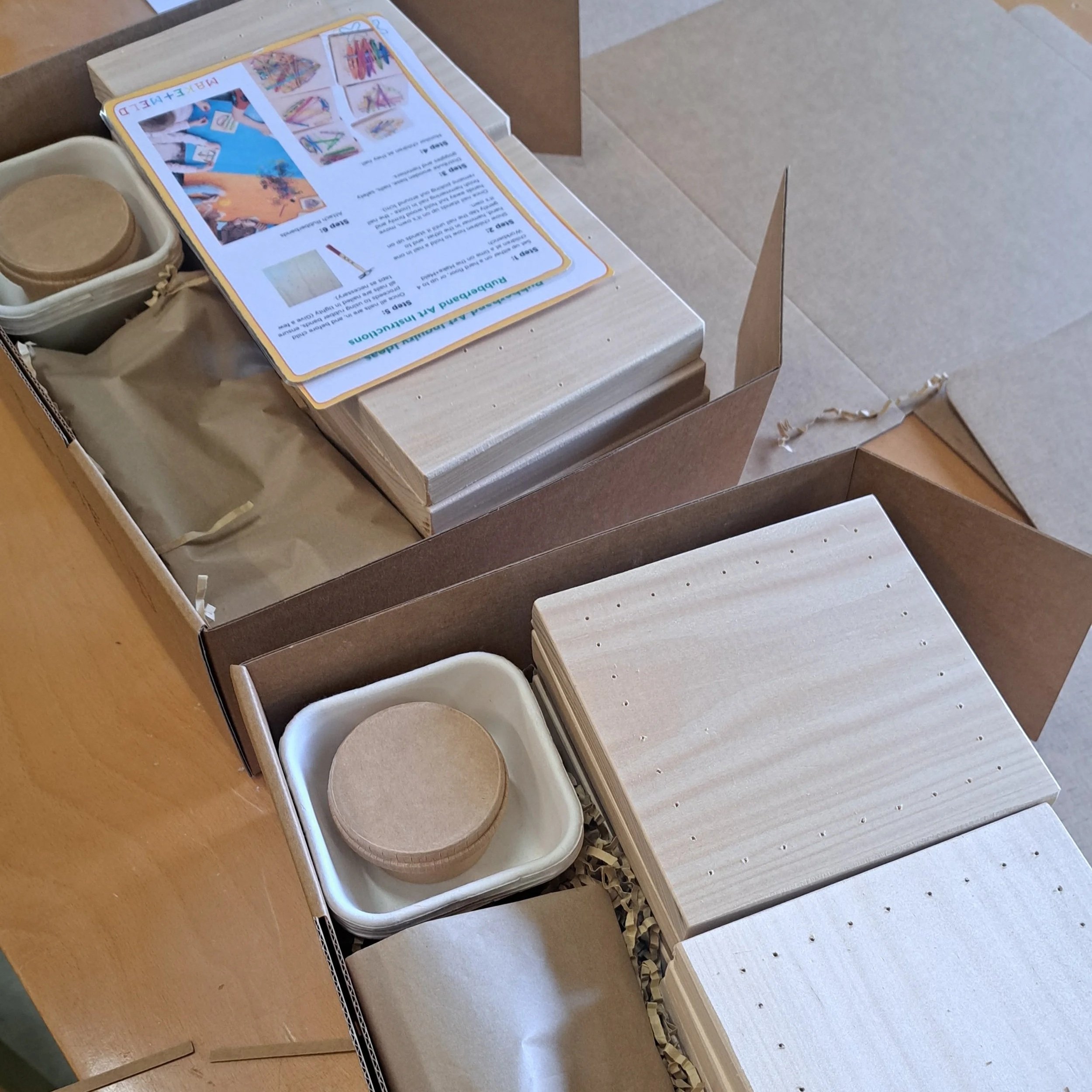 Unboxed wooden craft supplies, including wooden plates, a small wooden container, and instructional papers, arranged in a cardboard box.