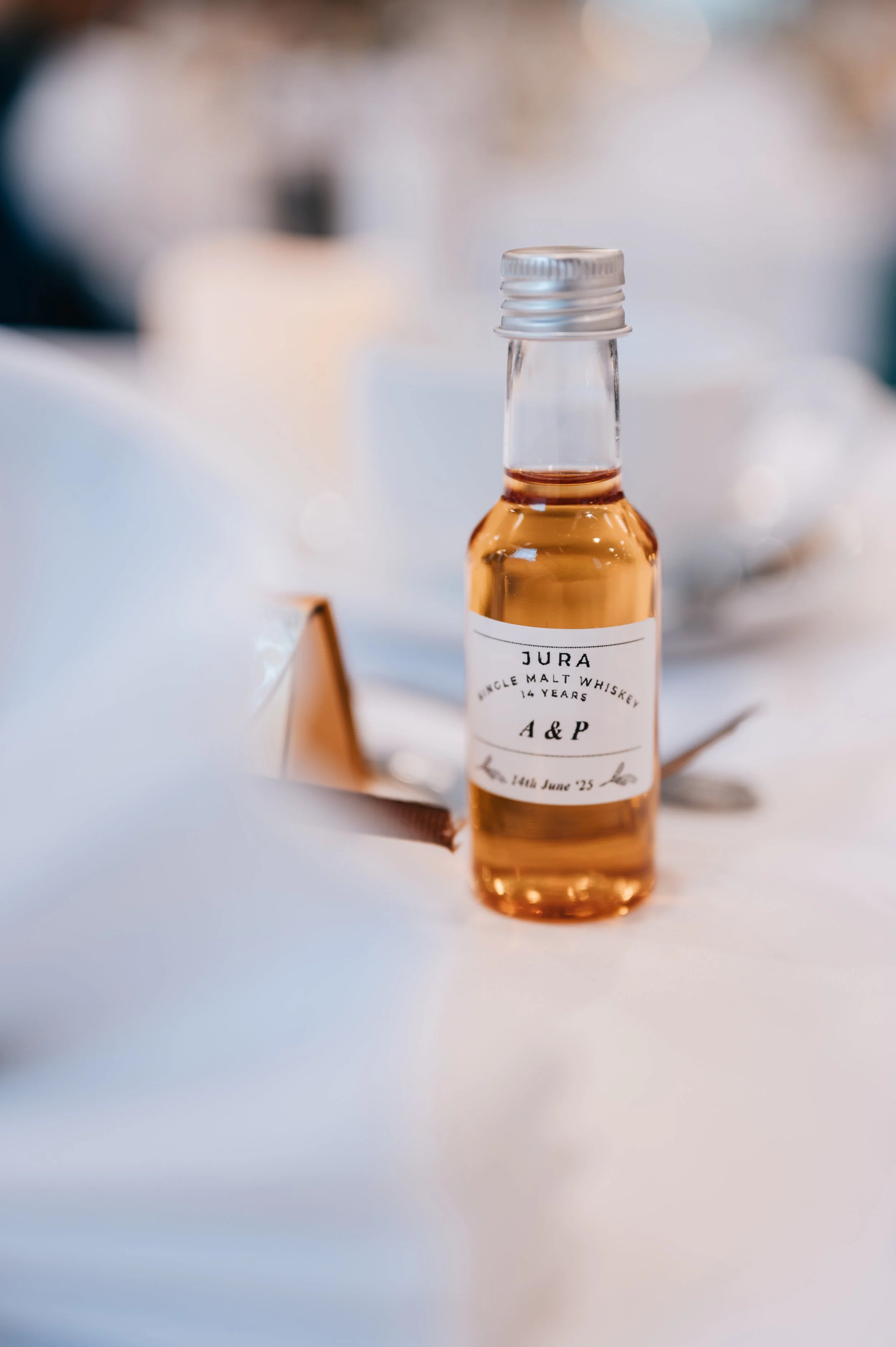 Small bottle of amber-colored liquor with a white label, placed on a white tablecloth during a formal event.