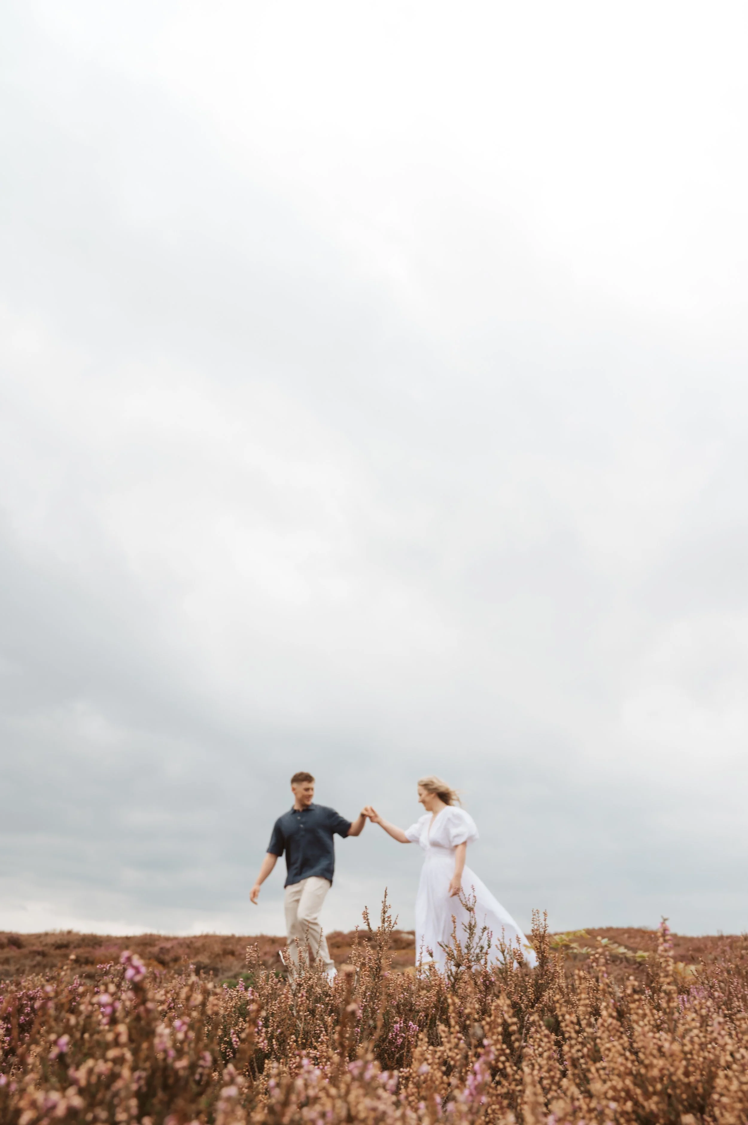 A couple dancing and holding hands in a field of pink flowers under a cloudy sky.
