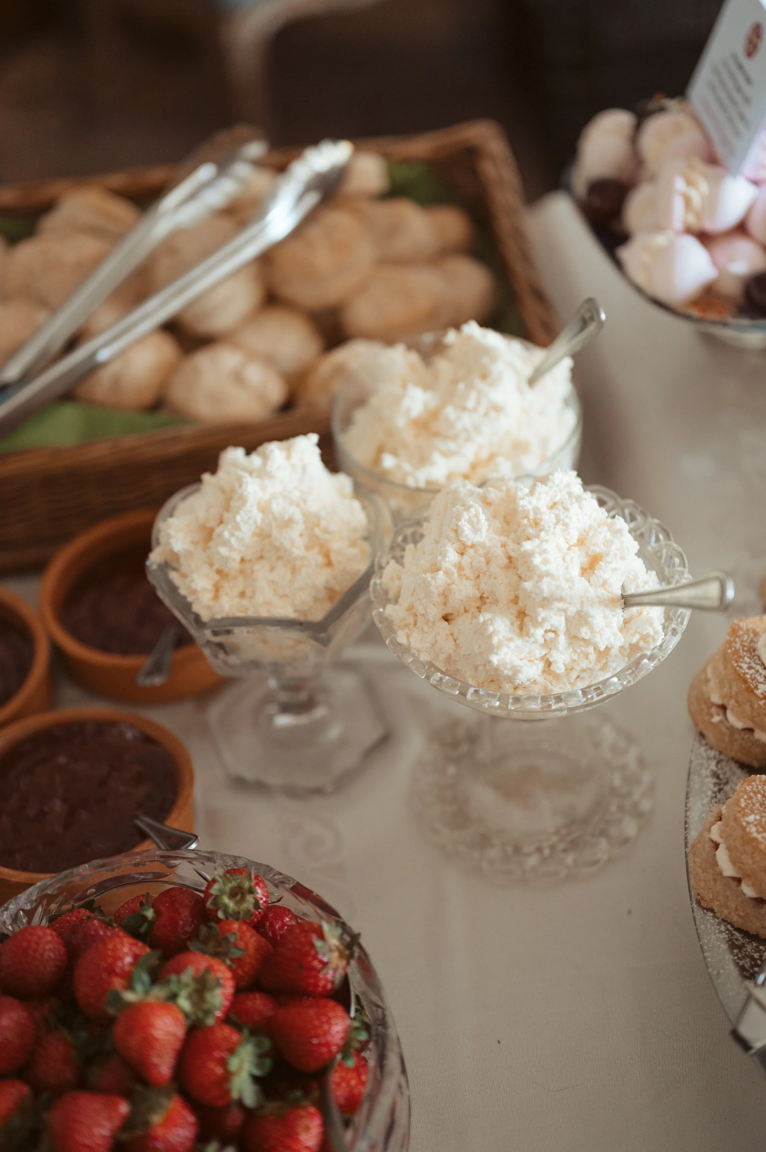 Assorted desserts, including bowls of vanilla ice cream, strawberries, and small tarts, on a white table.