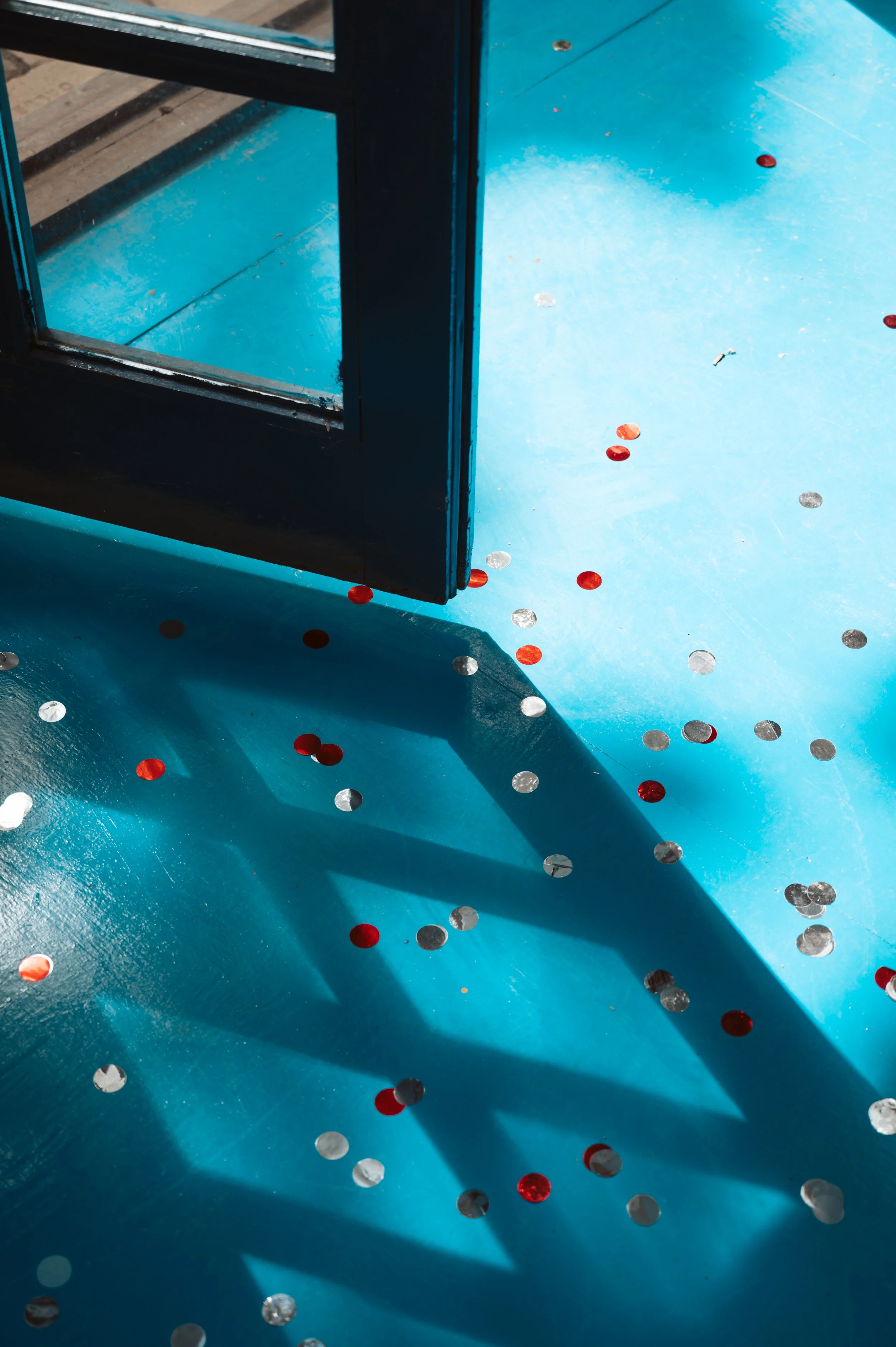Confetti scattered on a bright blue floor next to a partially open glass door casting a shadow.