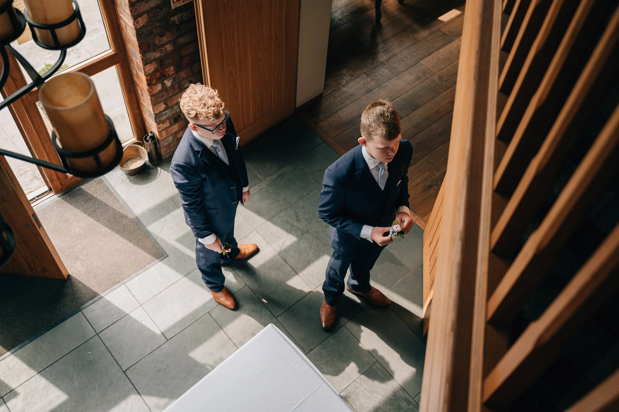 Two young men in suits standing in an entryway, one holding flowers, another looking at the door.