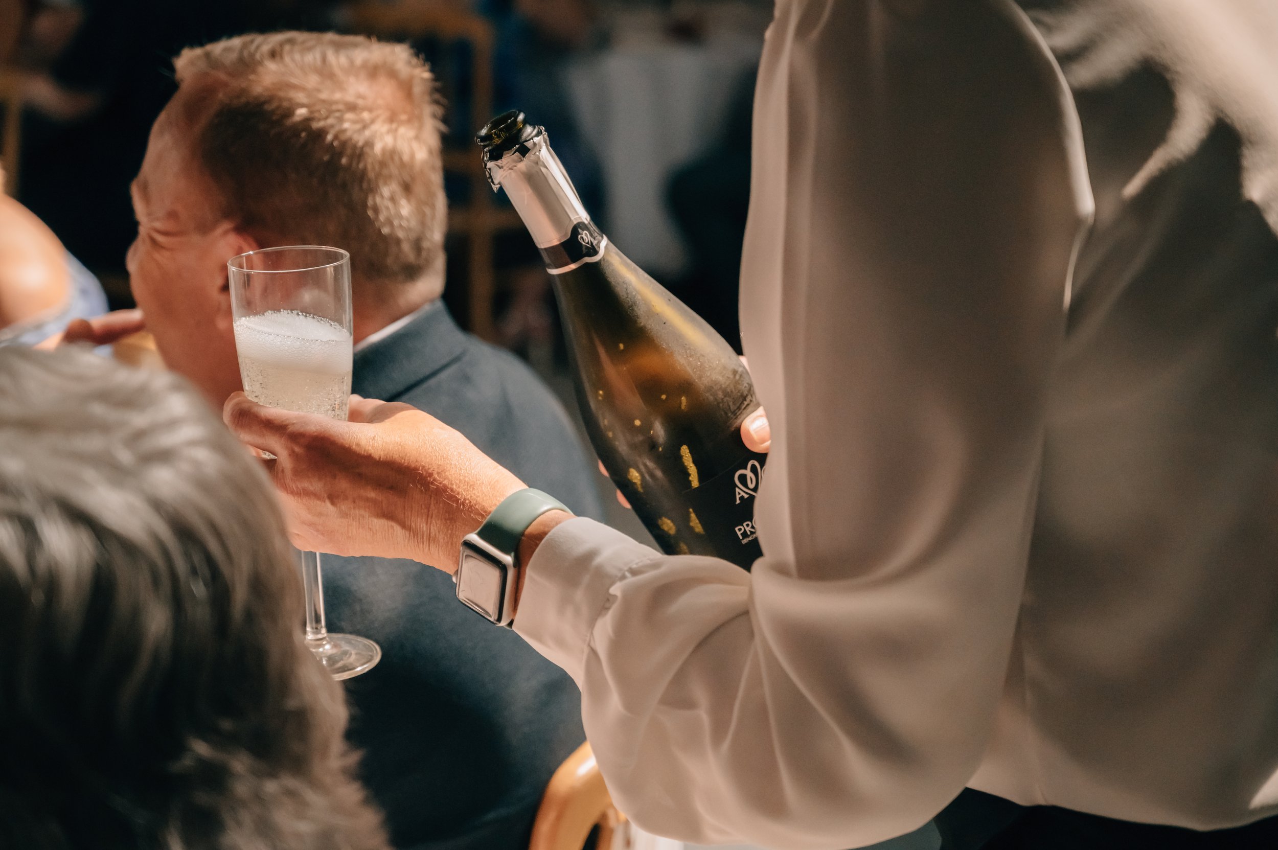 Person pouring champagne into a wine glass at a social gathering.