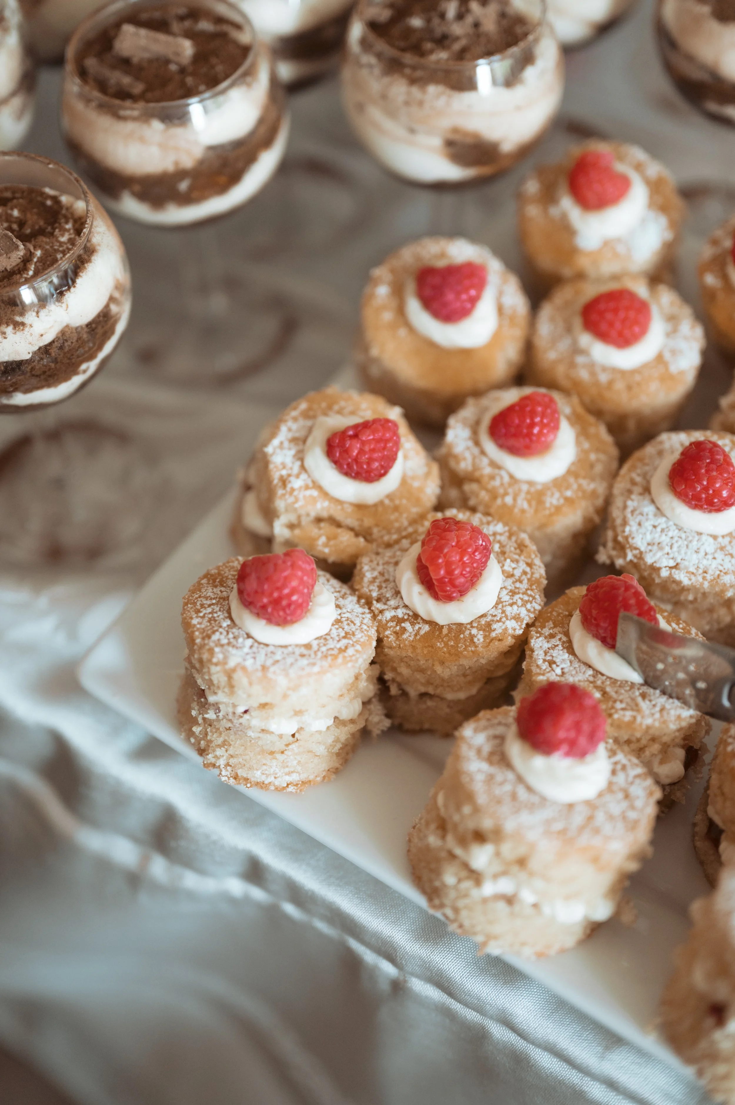 Assorted dessert appetizers, including raspberry-topped mini cakes and chocolate mousse cups, on a white serving platter.