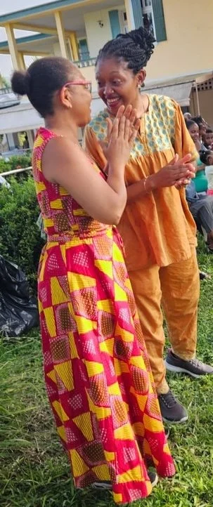 Afrobudgetingirl et sa mère partagent un moment de joie, souriantes et se tenant la main. Elles célèbrent quelque chose ou partagent un moment de bonheur. Les deux femmes sont vêtues de tenues traditionnelles africaines colorées.