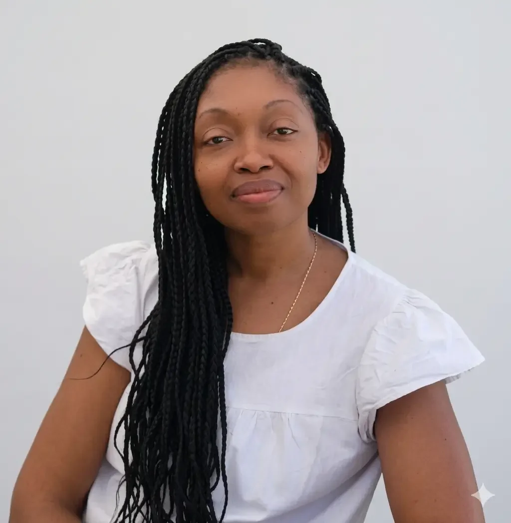 Ingrid Francisque, Founder of AfroBudgetinGirl is a black woman with long braided hair wearing a white blouse, seated against a plain white background. This is the portrait picture of "who i am" page for the founder.