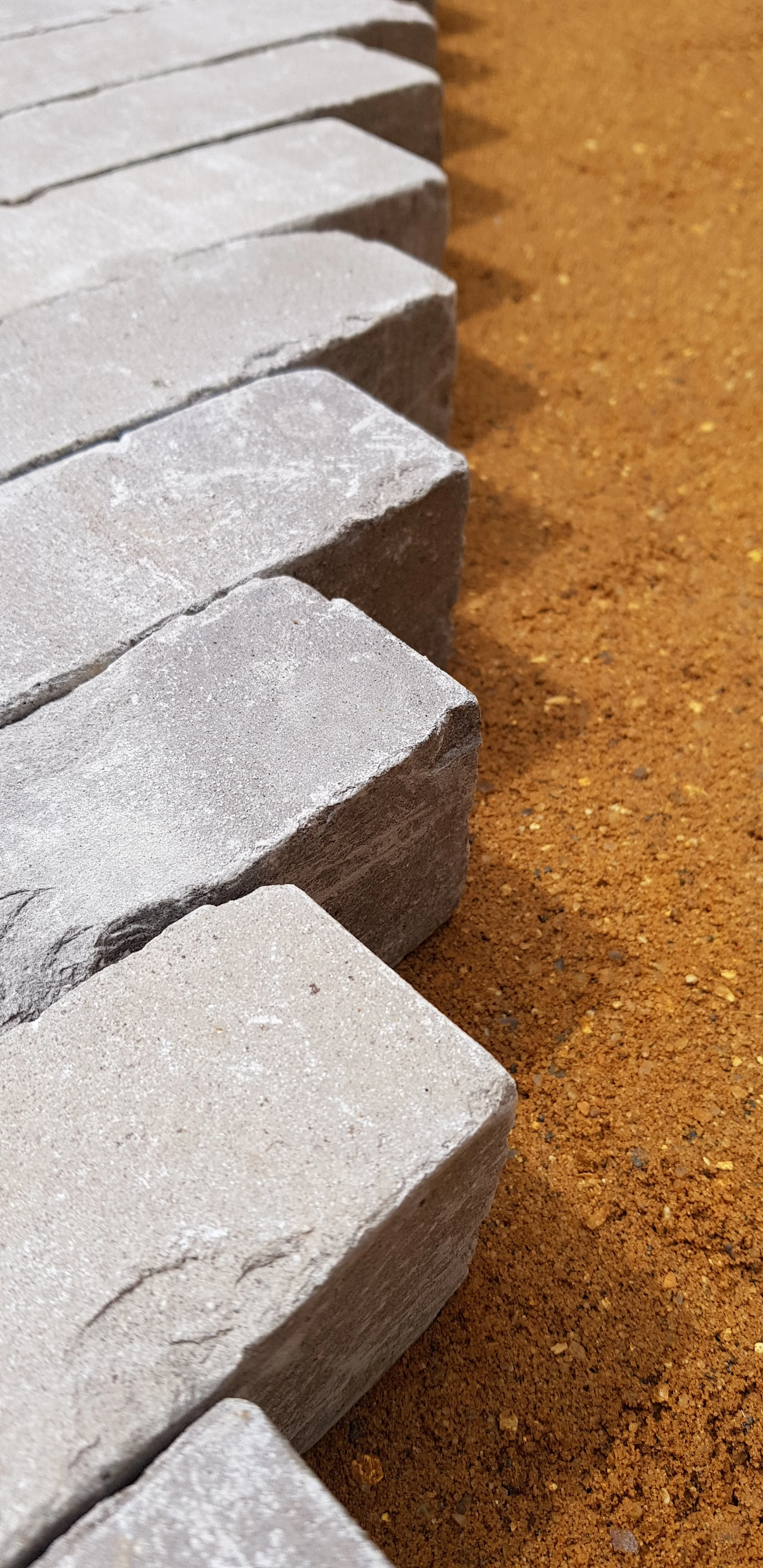 Close-up of gray brick pavers arranged in a row on a sand surface.