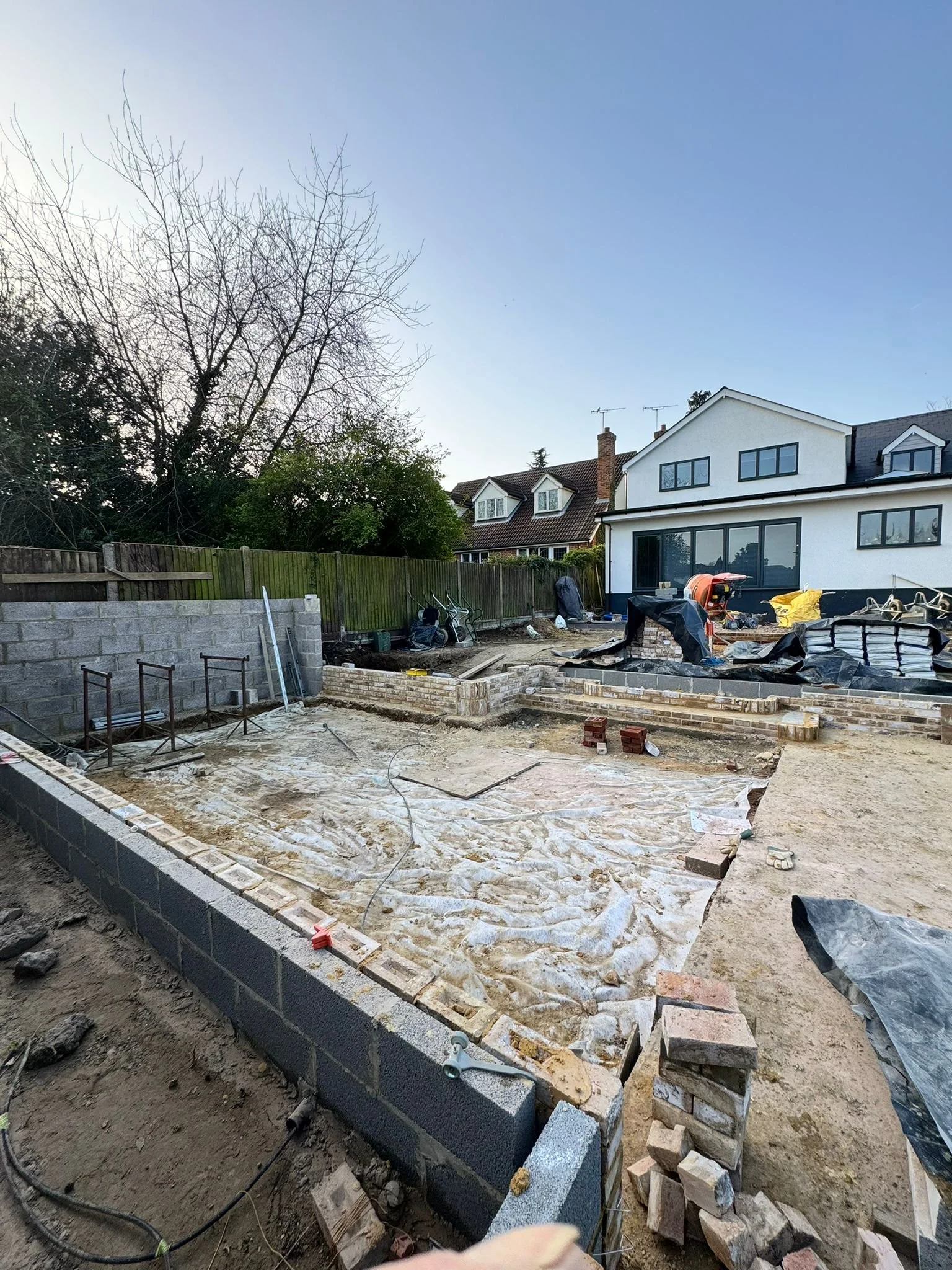 Backyard under construction with brick border, gravel, and construction tools and materials.