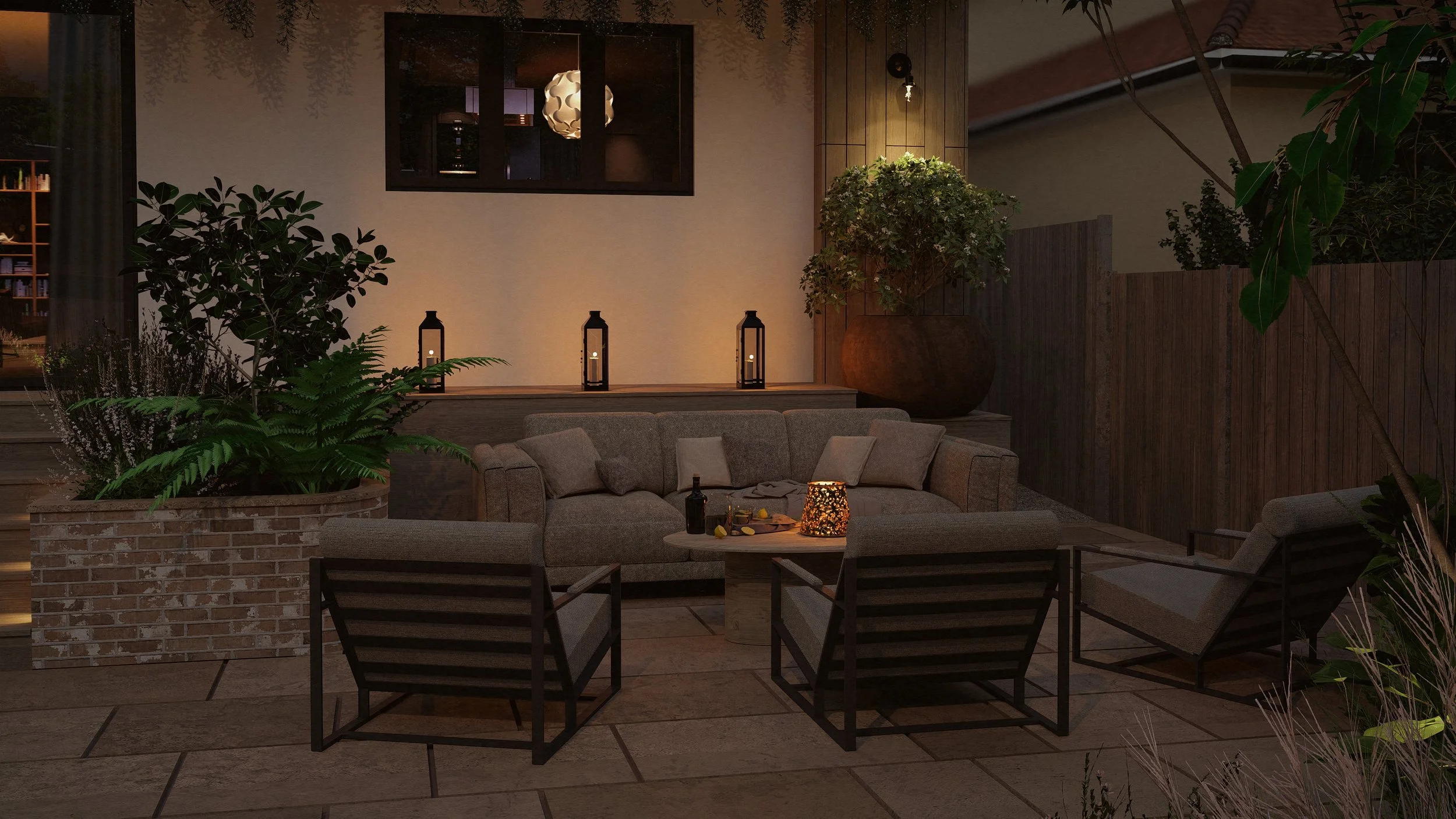 Outdoor patio at night with beige cushioned sofa, matching chairs, small wooden coffee table with lantern, candle, and drink, large potted plants, and decorative lanterns on the wall.