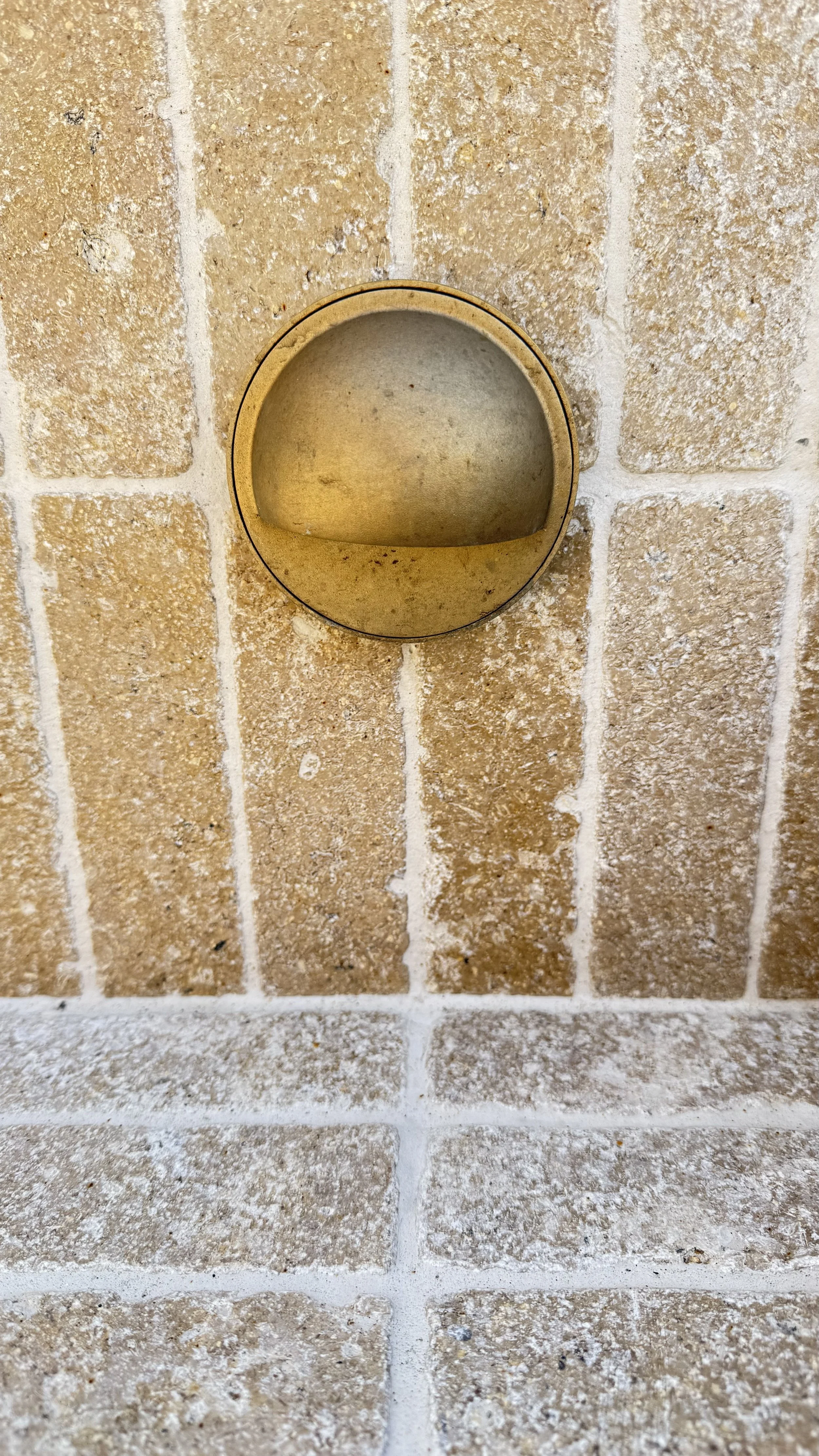A beige brick wall with an brass downlight.