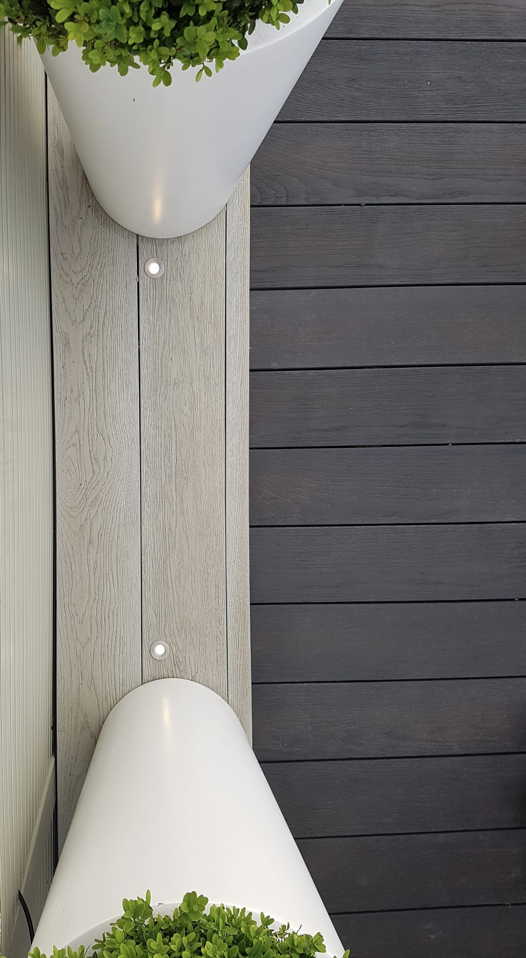 Top-down view of a white bathtub with a green potted plant inside, situated on a deck with light gray and dark gray wooden planks.