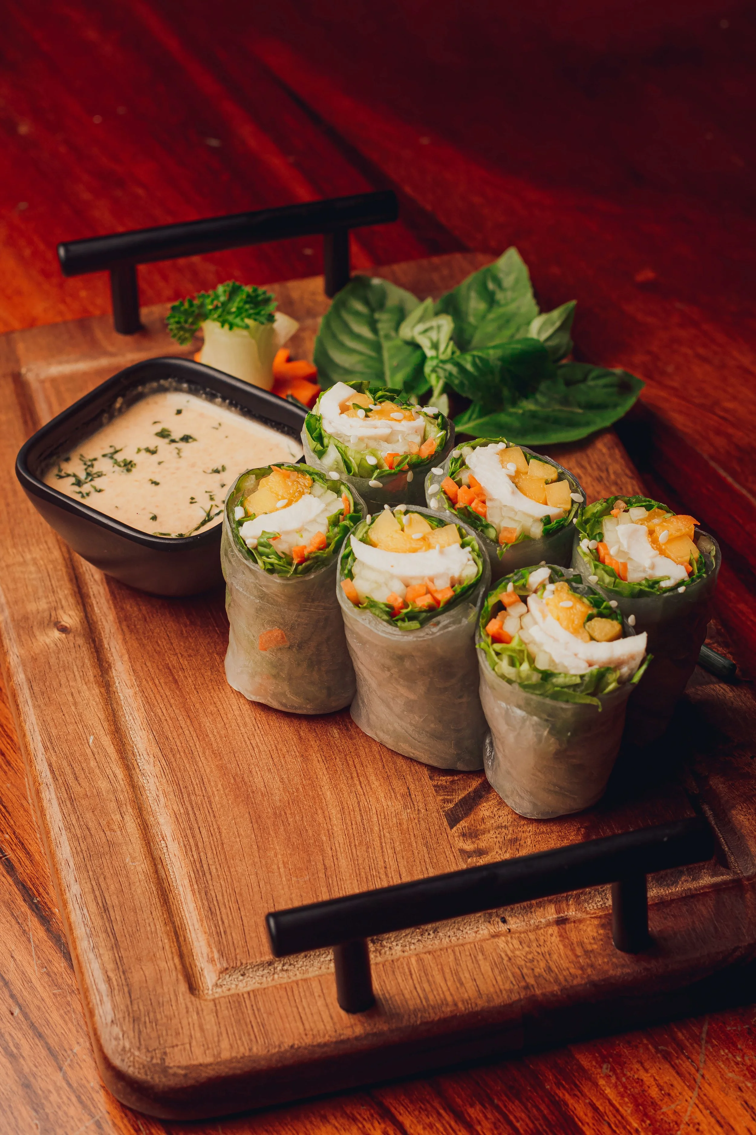 Fresh Vietnamese spring rolls filled with vegetables and seafood, served with a creamy dipping sauce, garnished with fresh herbs on a wooden platter.