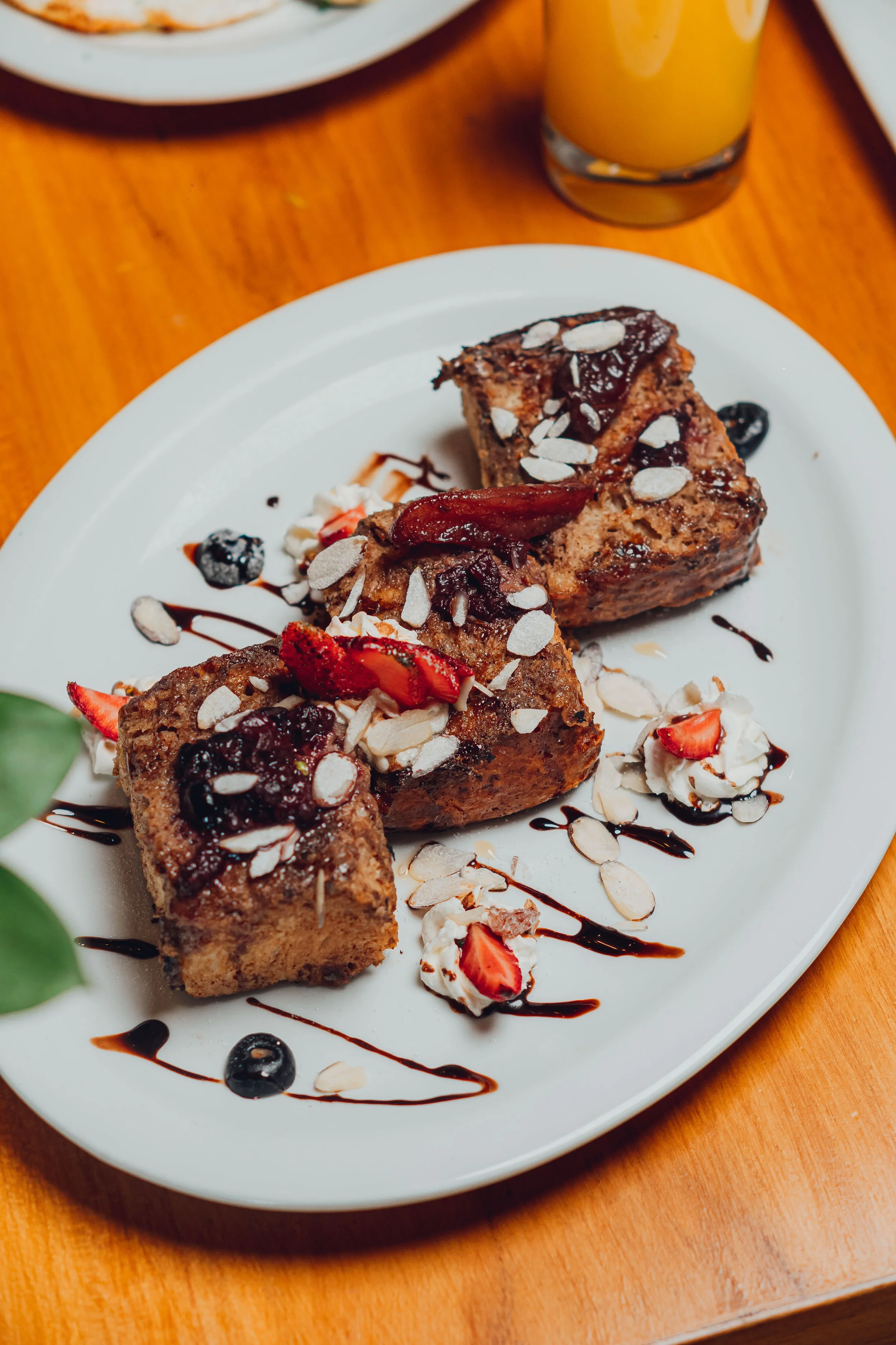 Three slices of cinnamon roll cake with strawberries, blueberries, whipped cream, sliced almonds, and chocolate sauce on a white plate.
