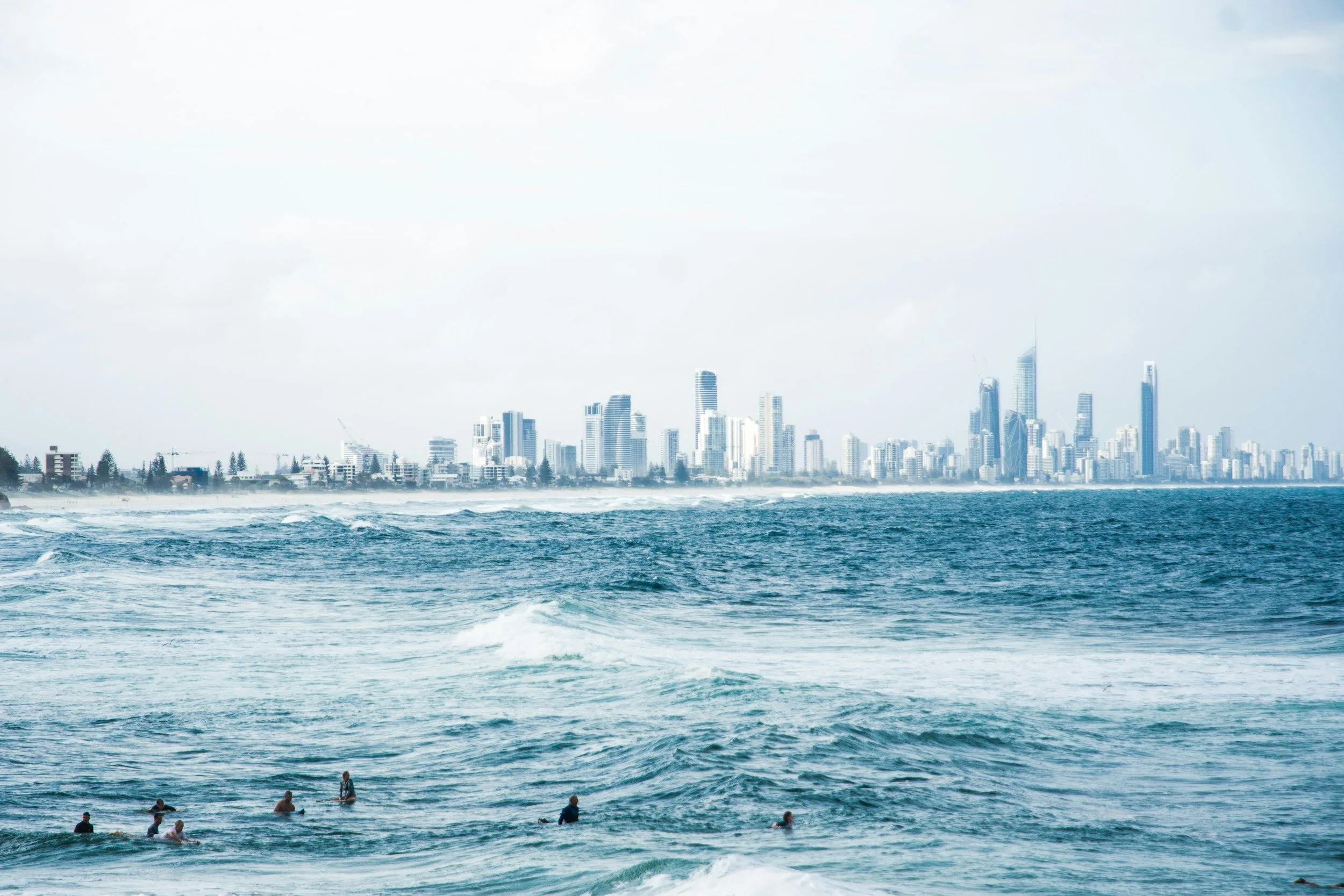 View of Gold Coast skyline across the ocean with waves and people swimming.