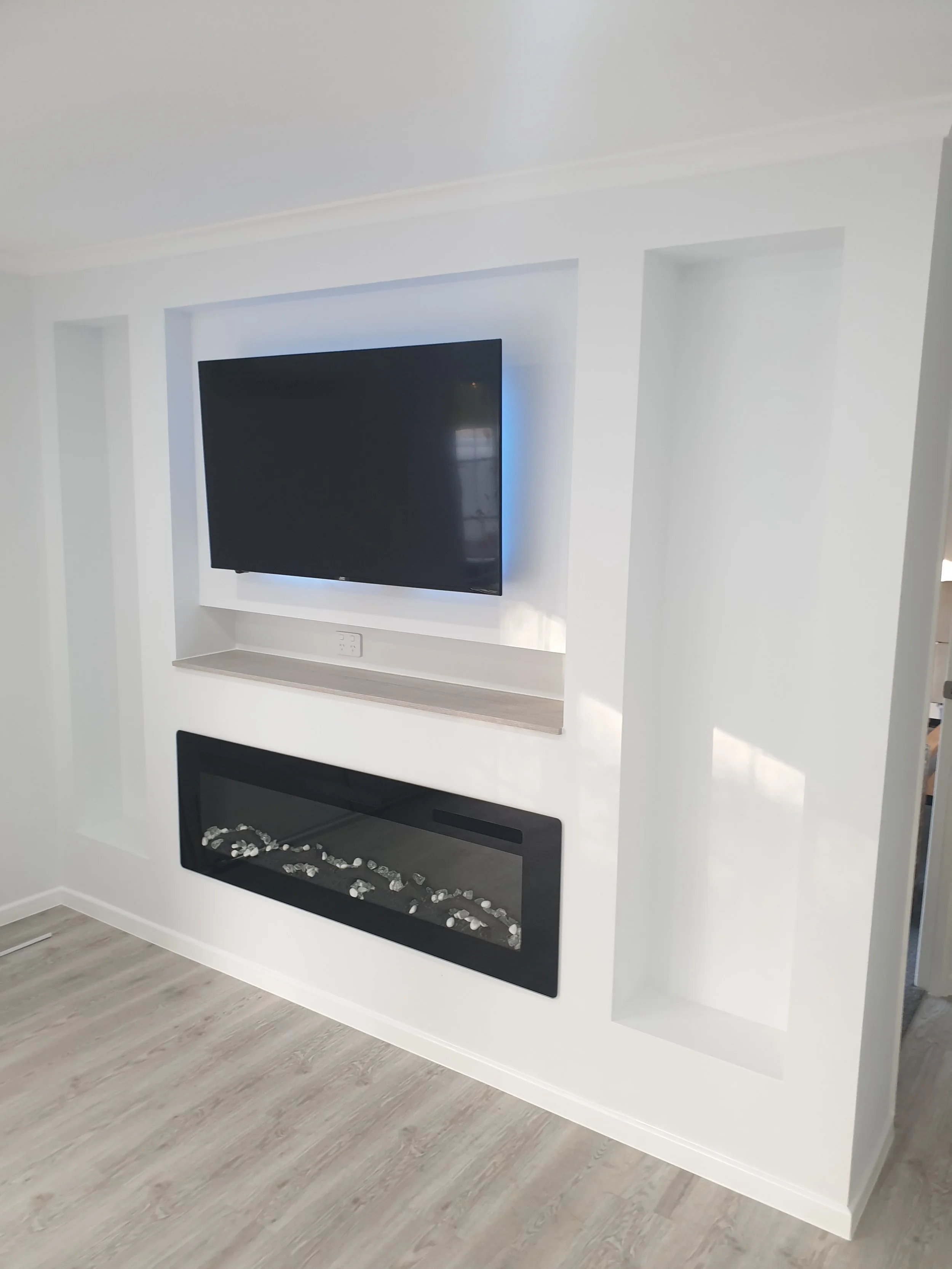 Living room wall with a mounted flat-screen TV above a built-in electric fireplace with decorative stones.