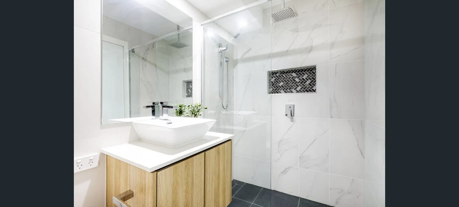 Modern bathroom with a white vessel sink on a wooden vanity, a large mirror, and a walk-in shower with glass enclosure and rainfall showerhead.