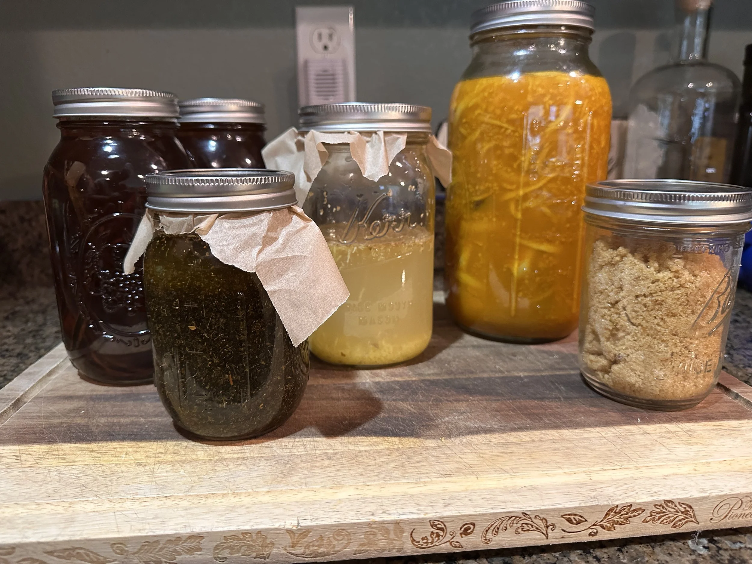 Assorted homemade jams and preserves in glass jars on a wooden cutting board.