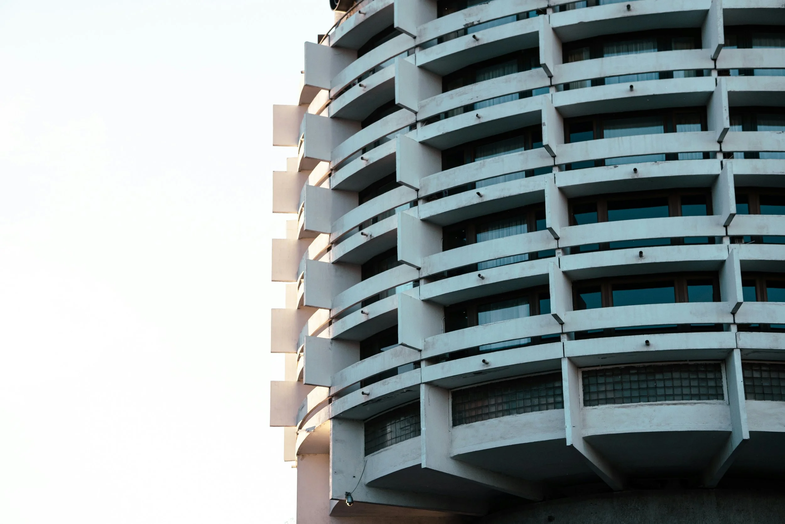 Close-up of a modern apartment building with rounded protruding balconies, partially lit by sunlight.