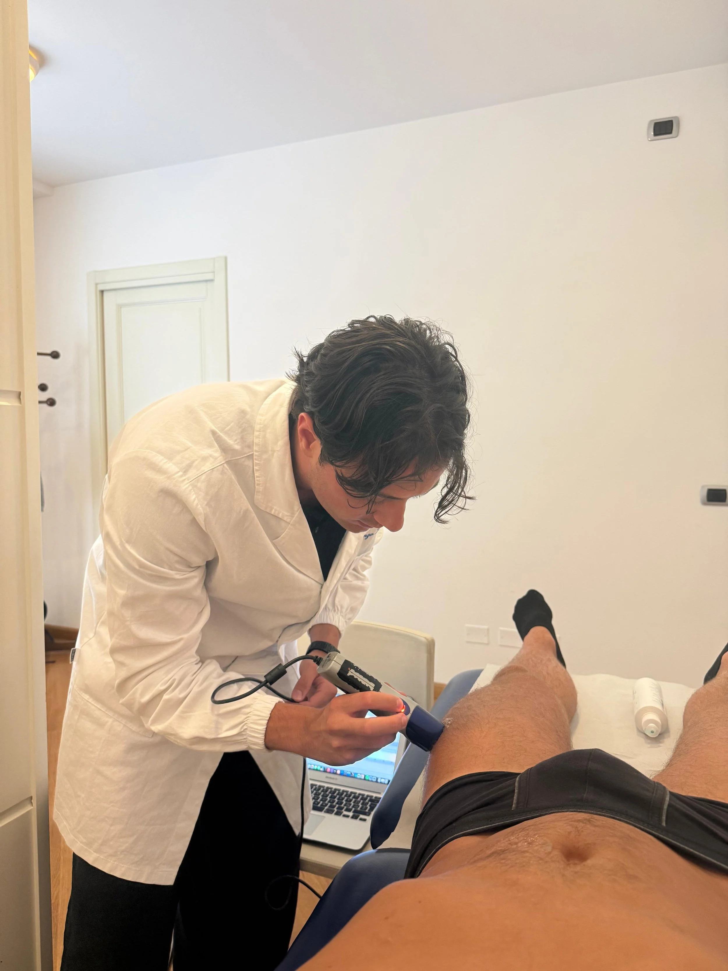 Un medico esamina un paziente con un dispositivo diagnostico, con un computer portatile aperto sulla sedia accanto.