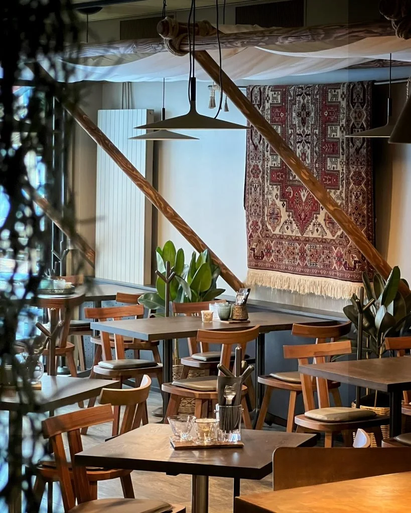 Un homme et une femme souriants, debout au bar, tenant chacun un verre de vin rouge, dans un bar avec étagères remplies de bouteilles d'alcool en arrière-plan.